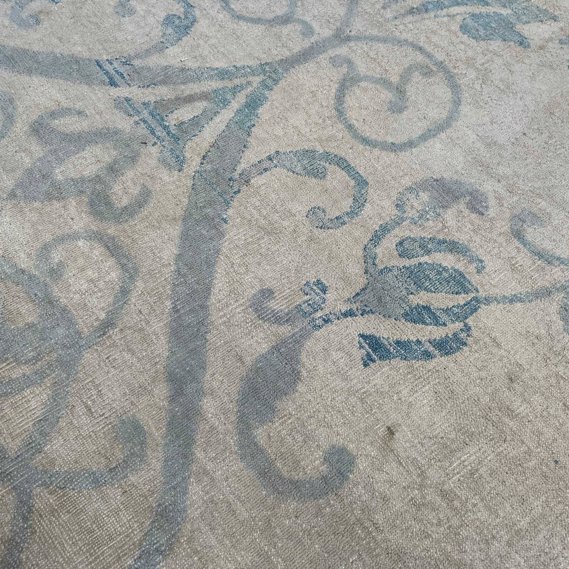 Close-up of a corner of an ornate, traditional Vintage rug with blue patterns on a beige background.