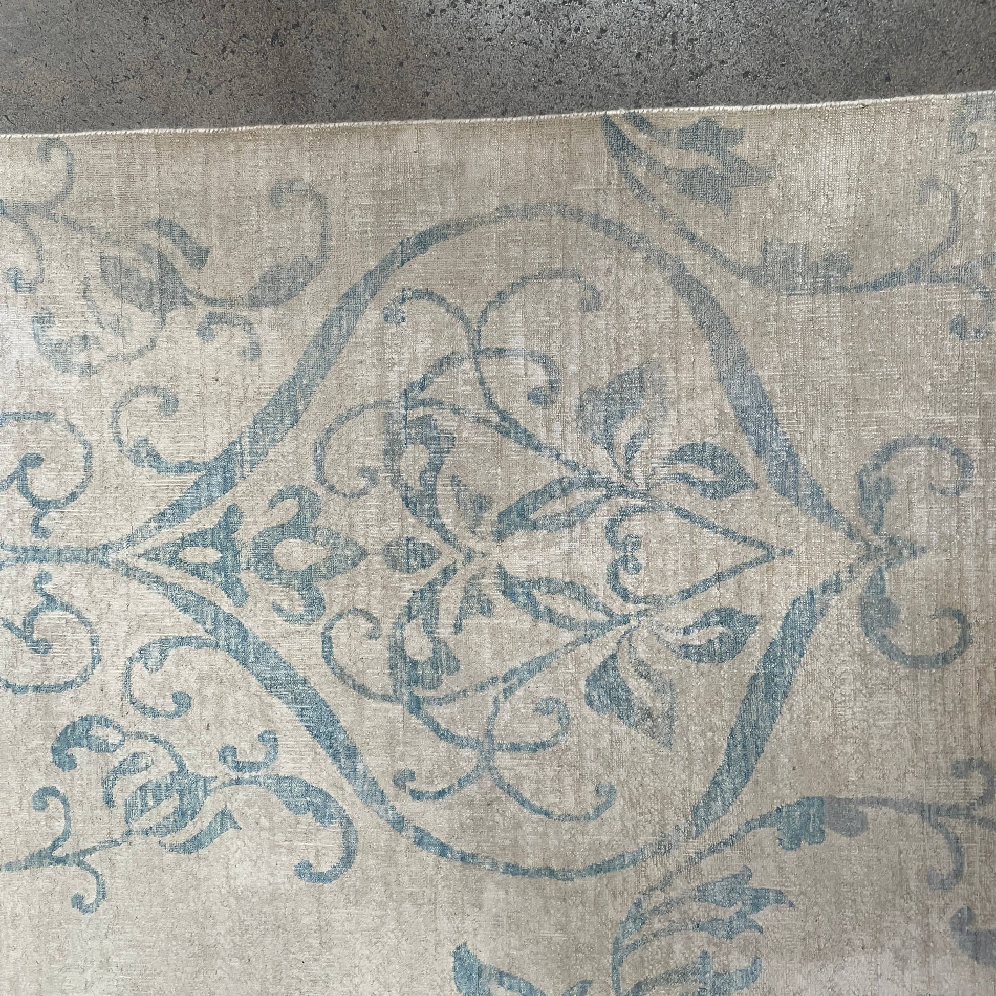 Close-up of a corner of an ornate, traditional Vintage rug with blue patterns on a beige background.