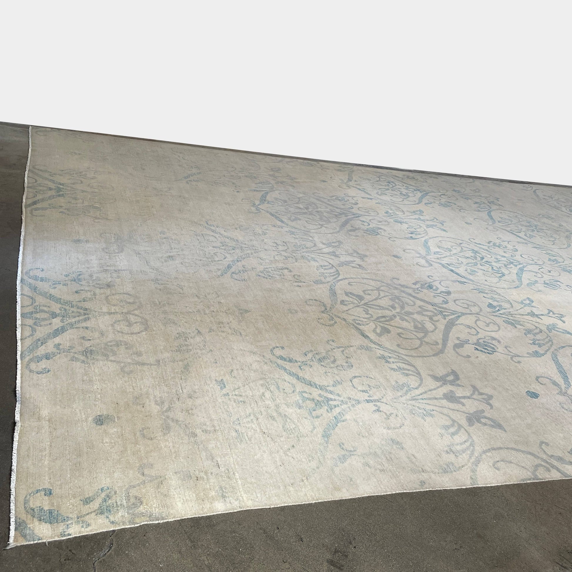 Close-up of a corner of an ornate, traditional Vintage rug with blue patterns on a beige background.