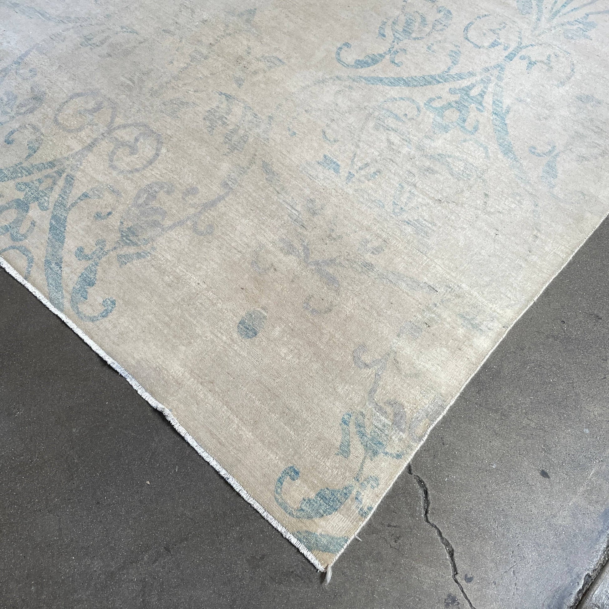 Close-up of a corner of an ornate, traditional Vintage rug with blue patterns on a beige background.
