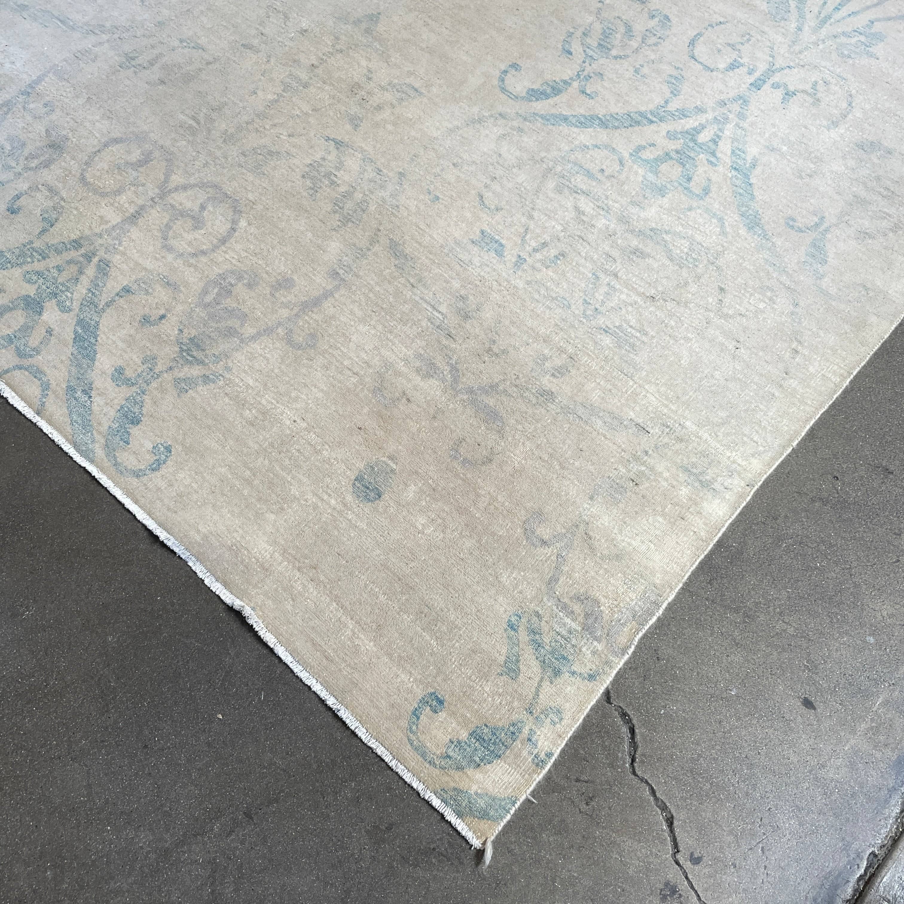Close-up of a corner of an ornate, traditional Vintage rug with blue patterns on a beige background.