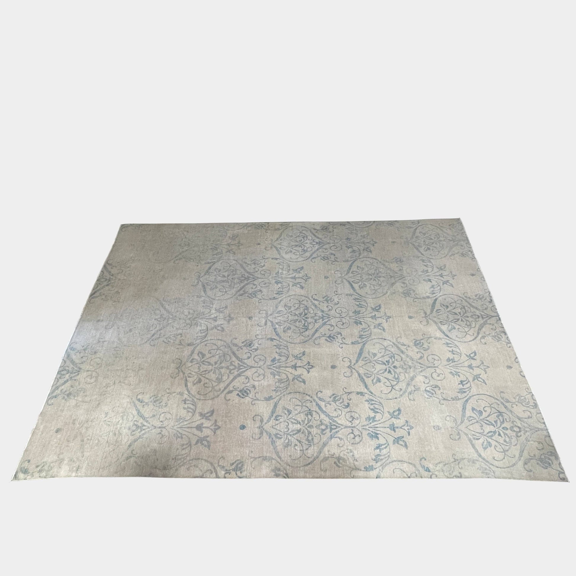 Close-up of a corner of an ornate, traditional Vintage rug with blue patterns on a beige background.