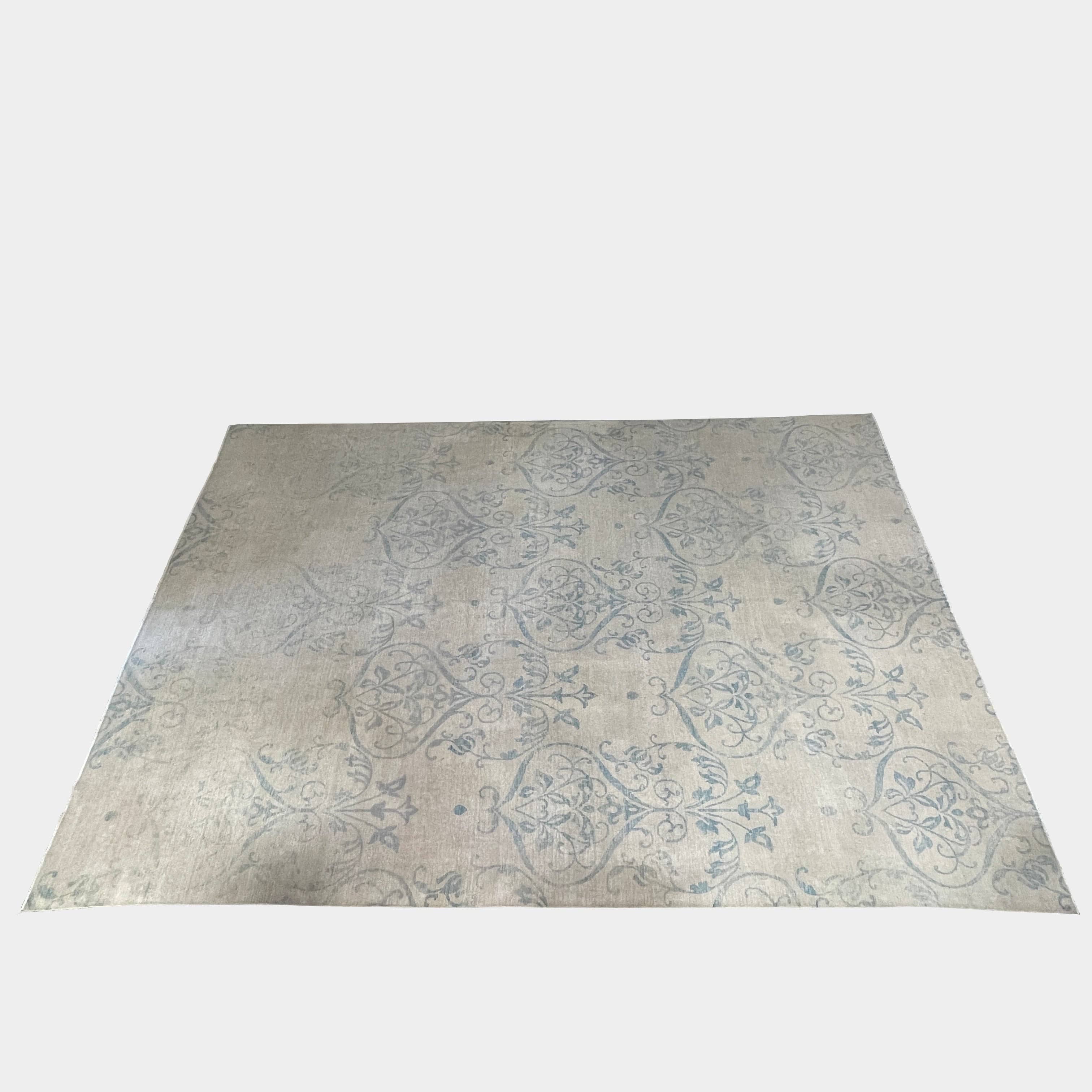 Close-up of a corner of an ornate, traditional Vintage rug with blue patterns on a beige background.