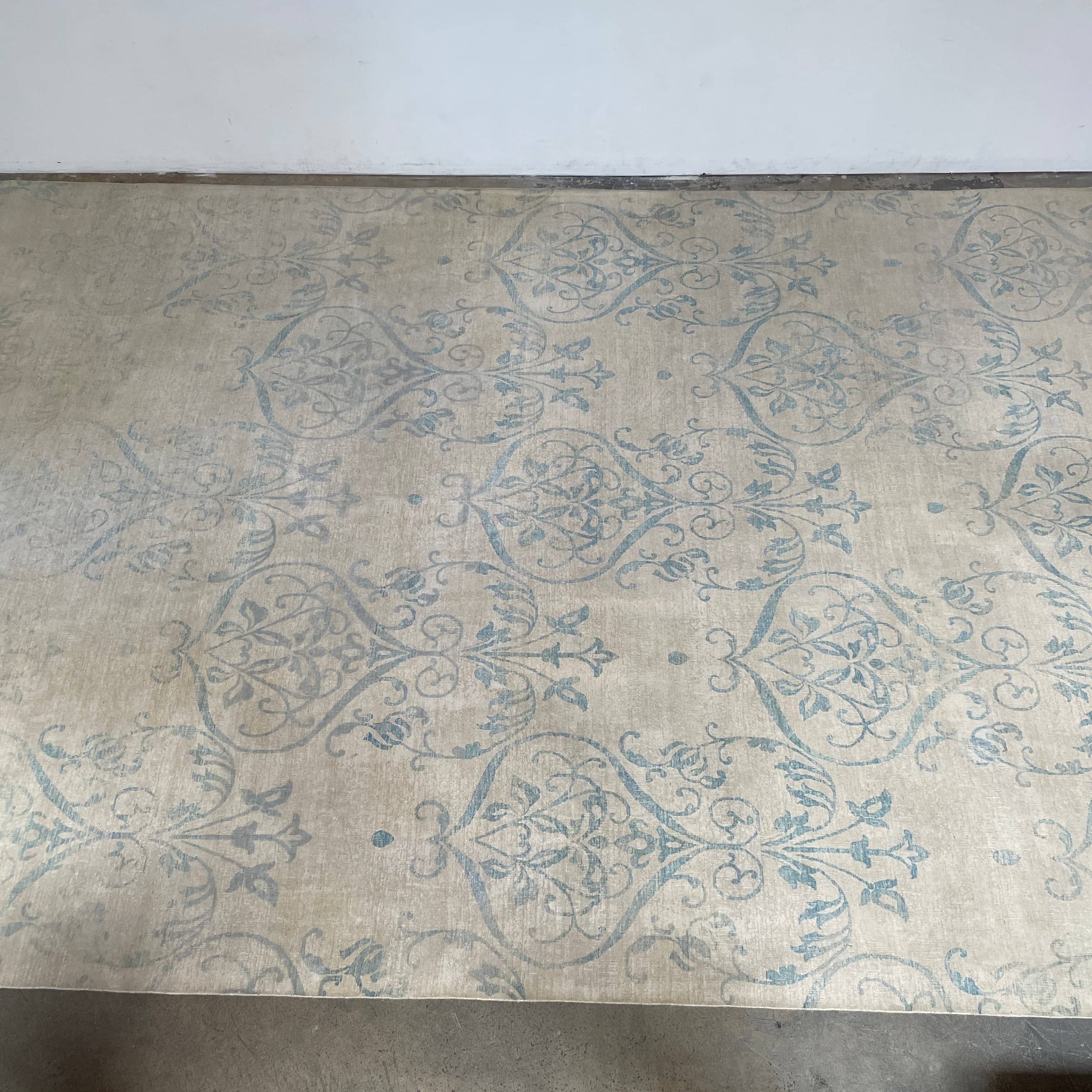 Close-up of a corner of an ornate, traditional Vintage rug with blue patterns on a beige background.