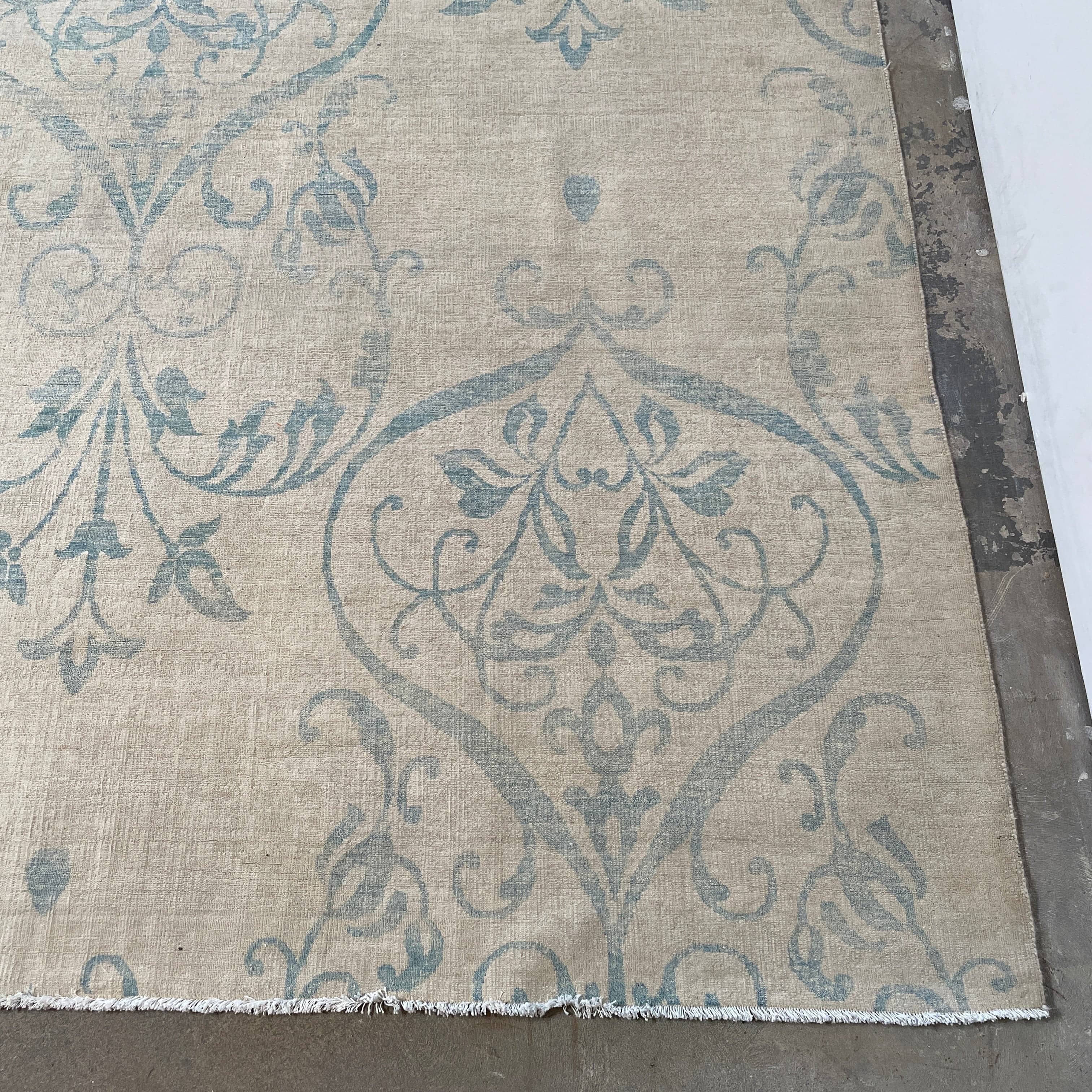 Close-up of a corner of an ornate, traditional Vintage rug with blue patterns on a beige background.