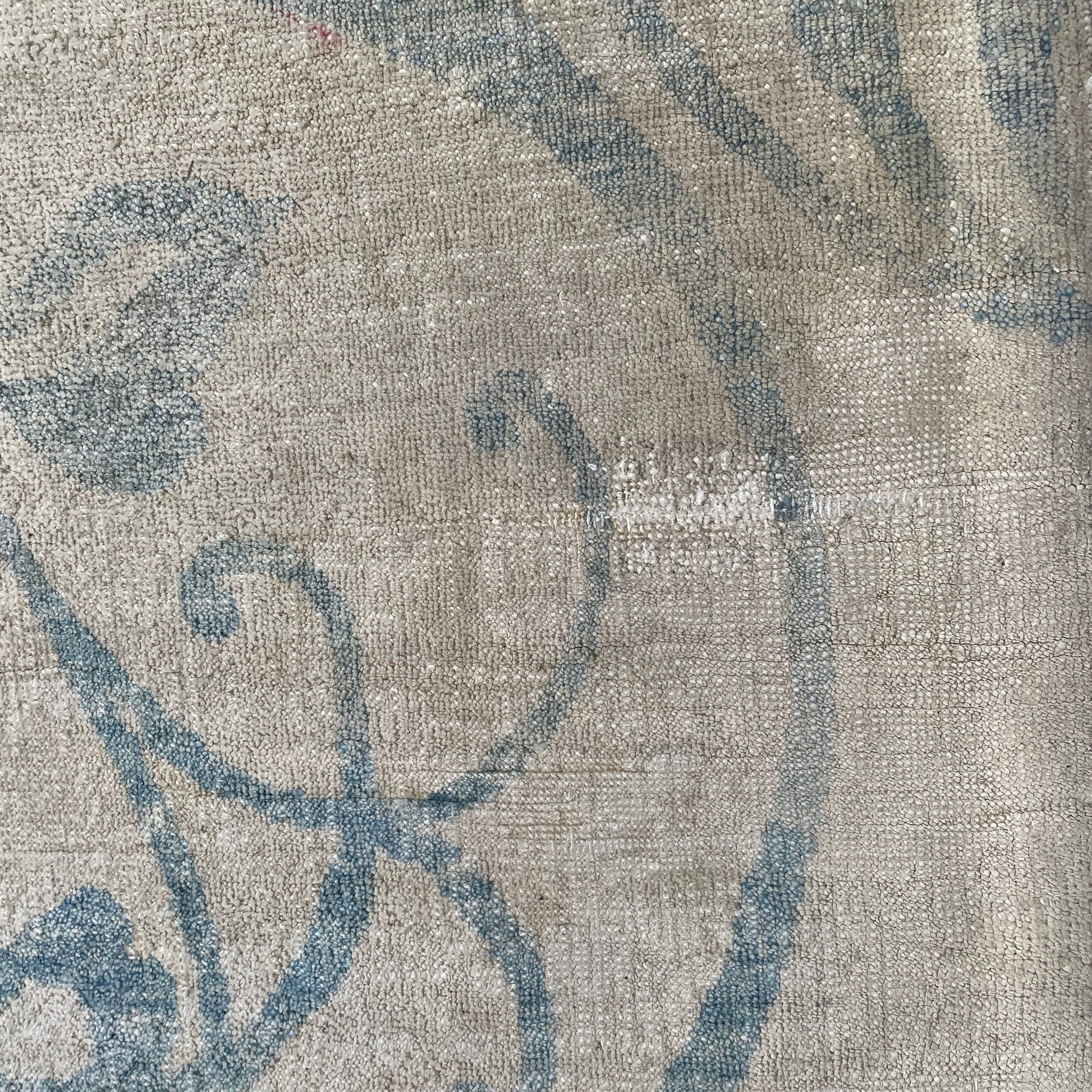 Close-up of a corner of an ornate, traditional Vintage rug with blue patterns on a beige background.