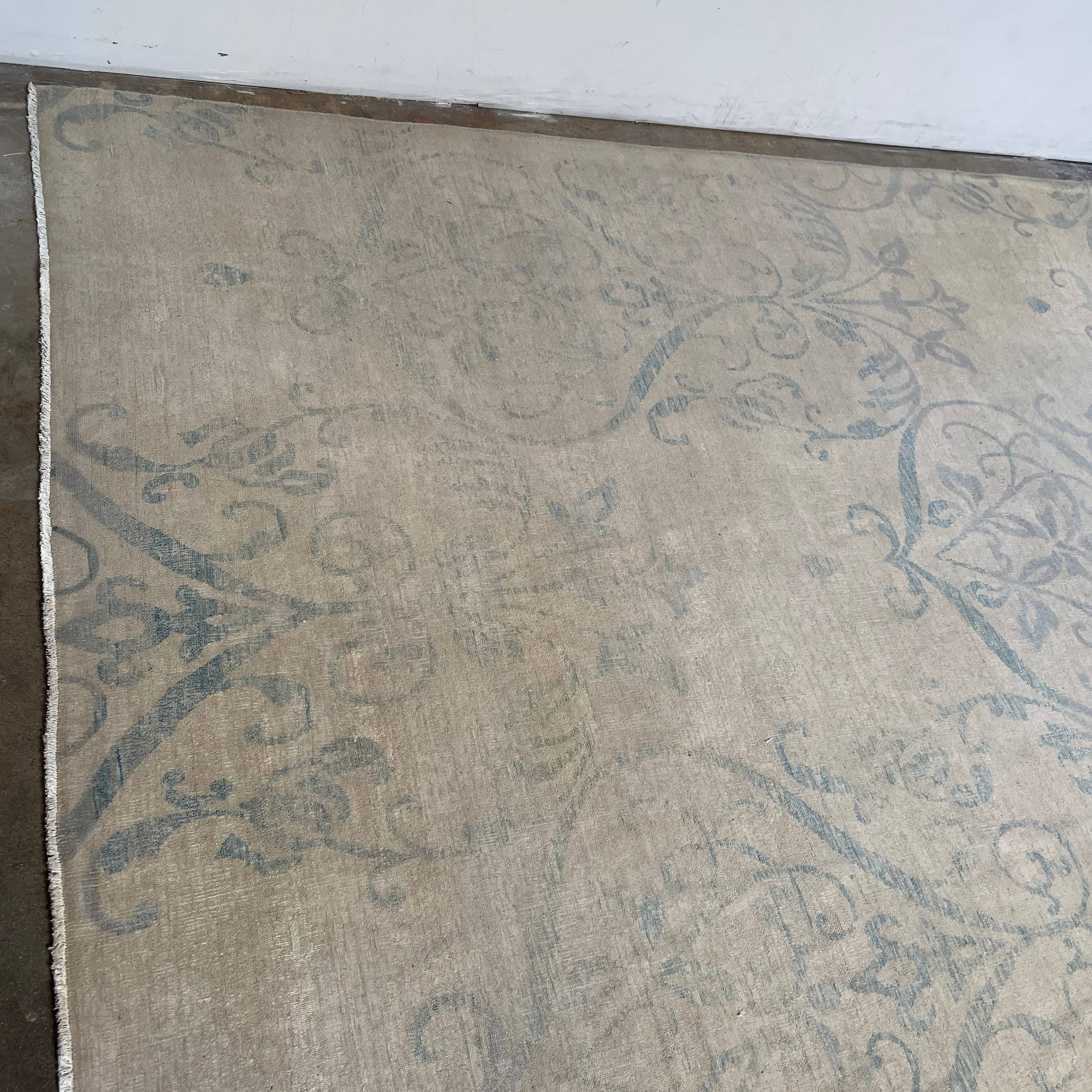 Close-up of a corner of an ornate, traditional Vintage rug with blue patterns on a beige background.