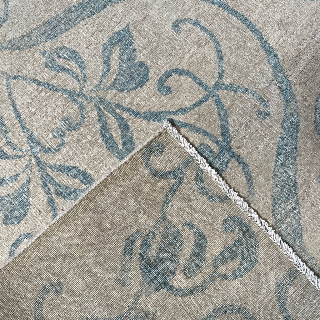 Close-up of a corner of an ornate, traditional Vintage rug with blue patterns on a beige background.