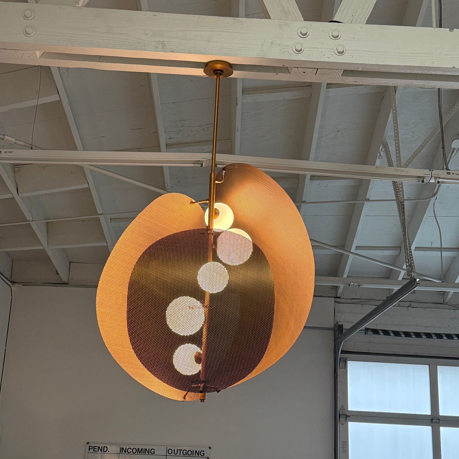 A modern chandelier with circular metal mesh panels and a central bulb hangs from a golden rod, reminiscent of the Studio M Chips 5-Light Vertical Pendant in Natural Aged Brass.
