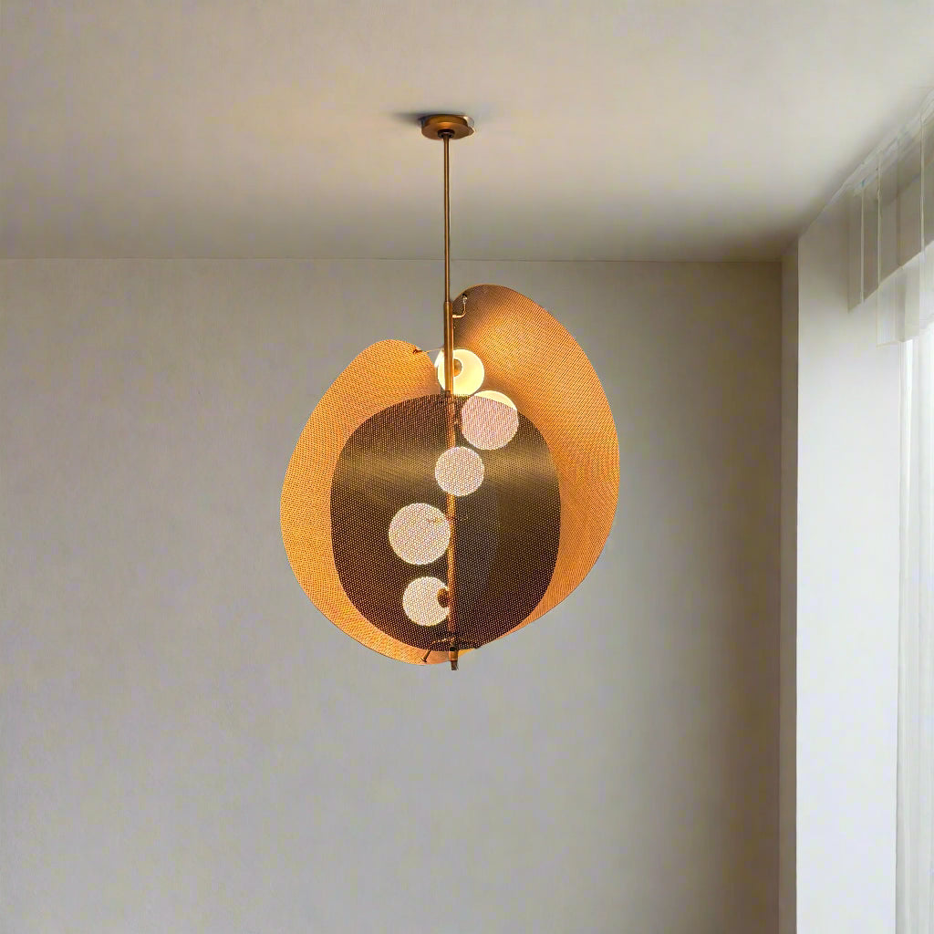 A modern chandelier with circular metal mesh panels and a central bulb hangs from a golden rod, reminiscent of the Studio M Chips 5-Light Vertical Pendant in Natural Aged Brass.