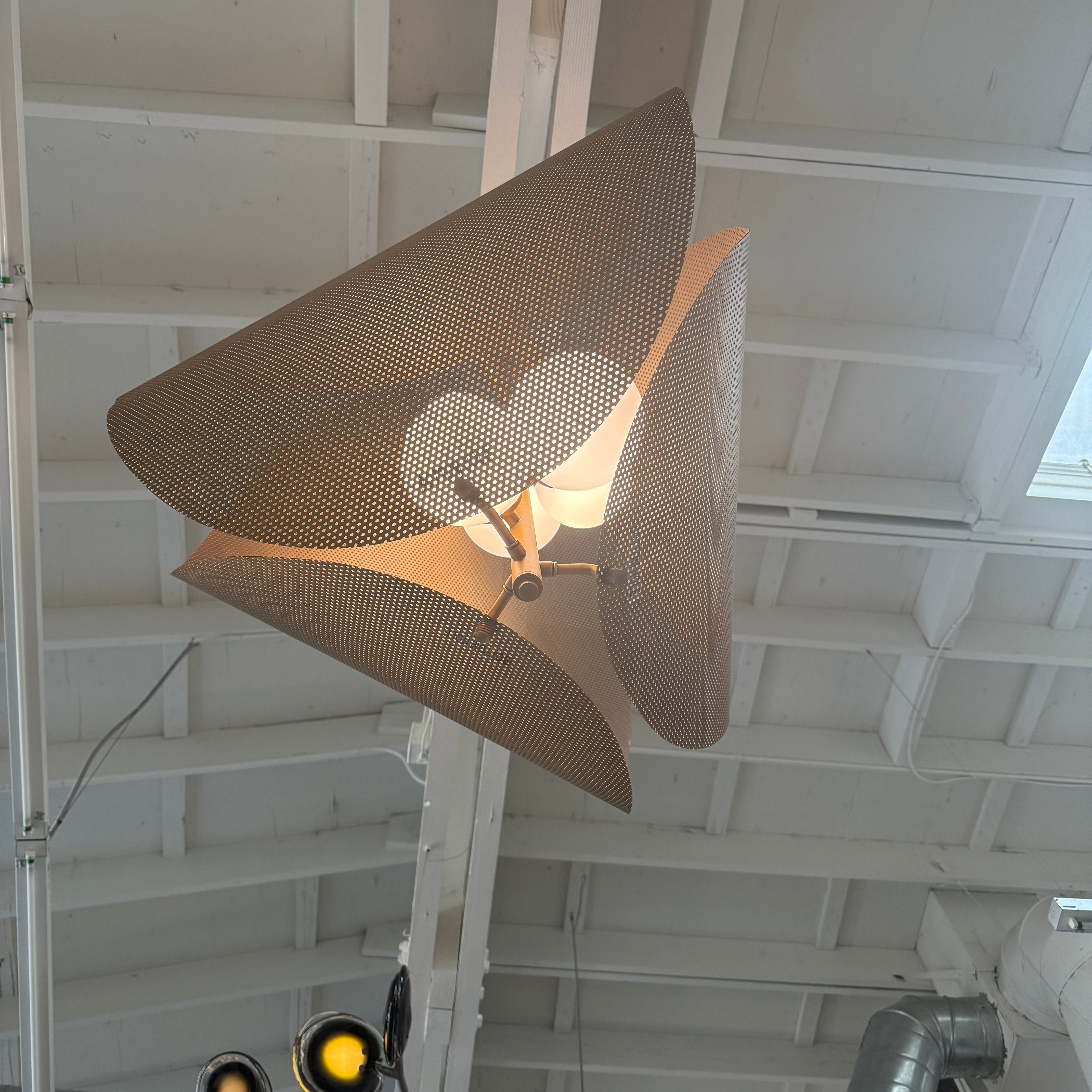 A modern chandelier with circular metal mesh panels and a central bulb hangs from a golden rod, reminiscent of the Studio M Chips 5-Light Vertical Pendant in Natural Aged Brass.