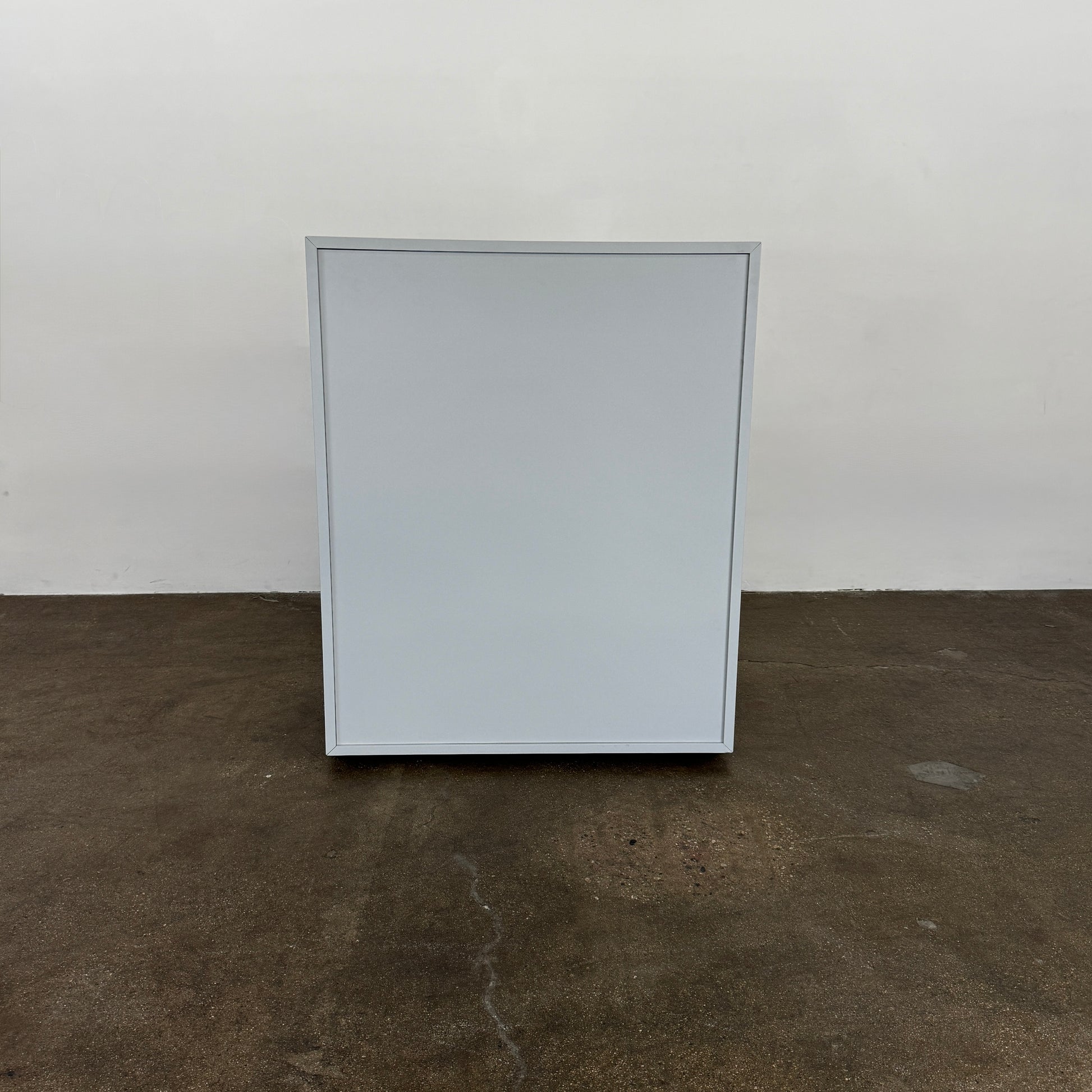 The Treku Lauki Tall Dresser by Treku, with a sleek lacquered finish and push-latch drawers—one partially open—stands on a concrete floor against a plain white wall.