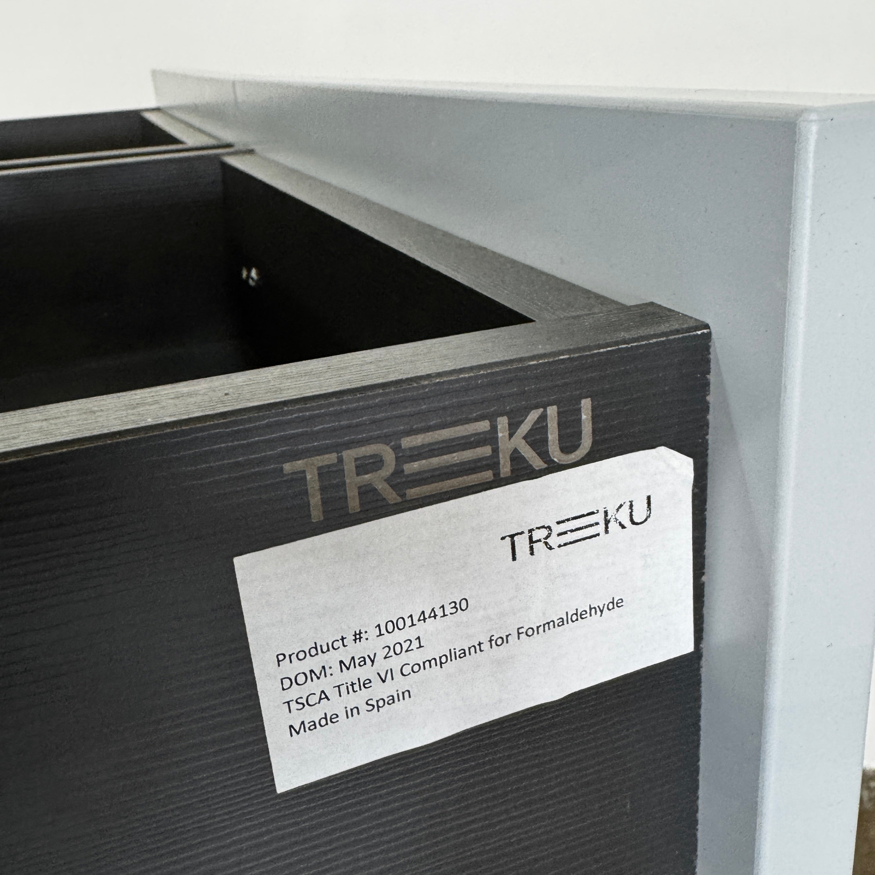 The Treku Lauki Tall Dresser by Treku, with a sleek lacquered finish and push-latch drawers—one partially open—stands on a concrete floor against a plain white wall.