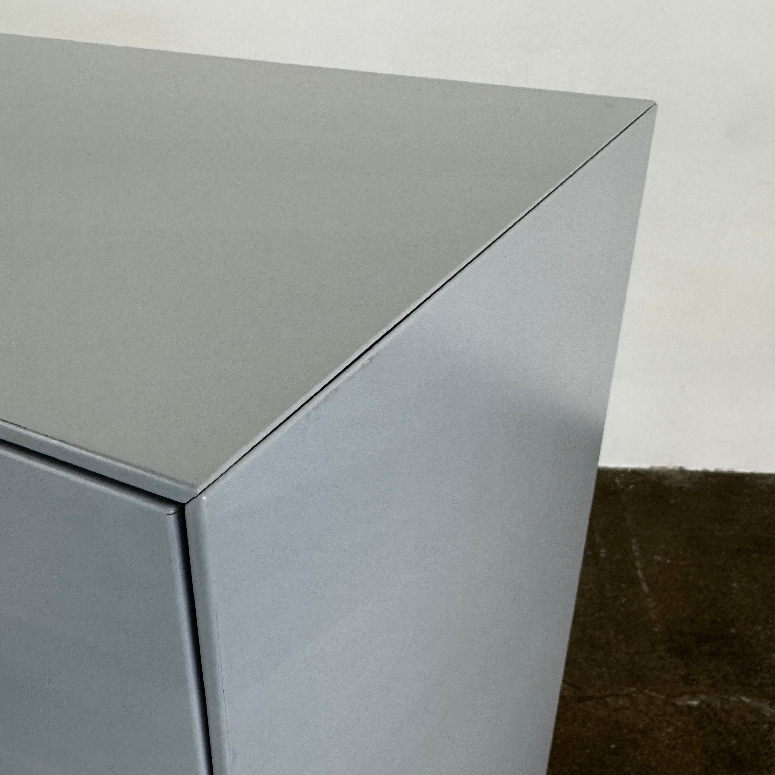 The Treku Lauki Tall Dresser by Treku, with a sleek lacquered finish and push-latch drawers—one partially open—stands on a concrete floor against a plain white wall.