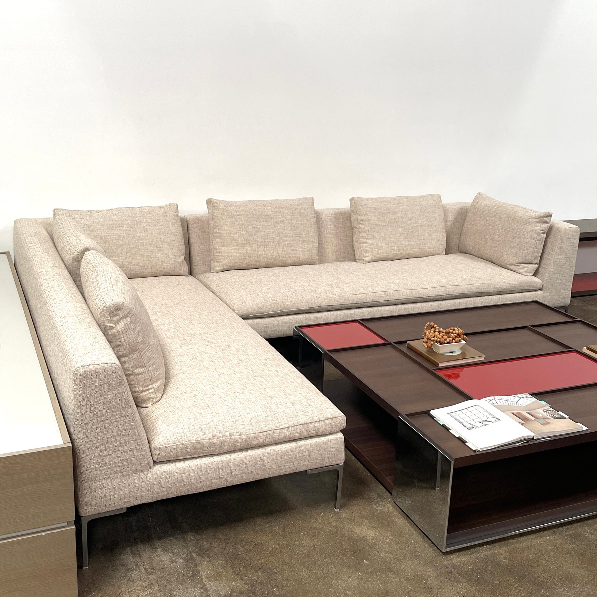 A beige B&B Italia Charles Sectional with five back cushions and metal legs sits on a concrete floor against a plain white wall.