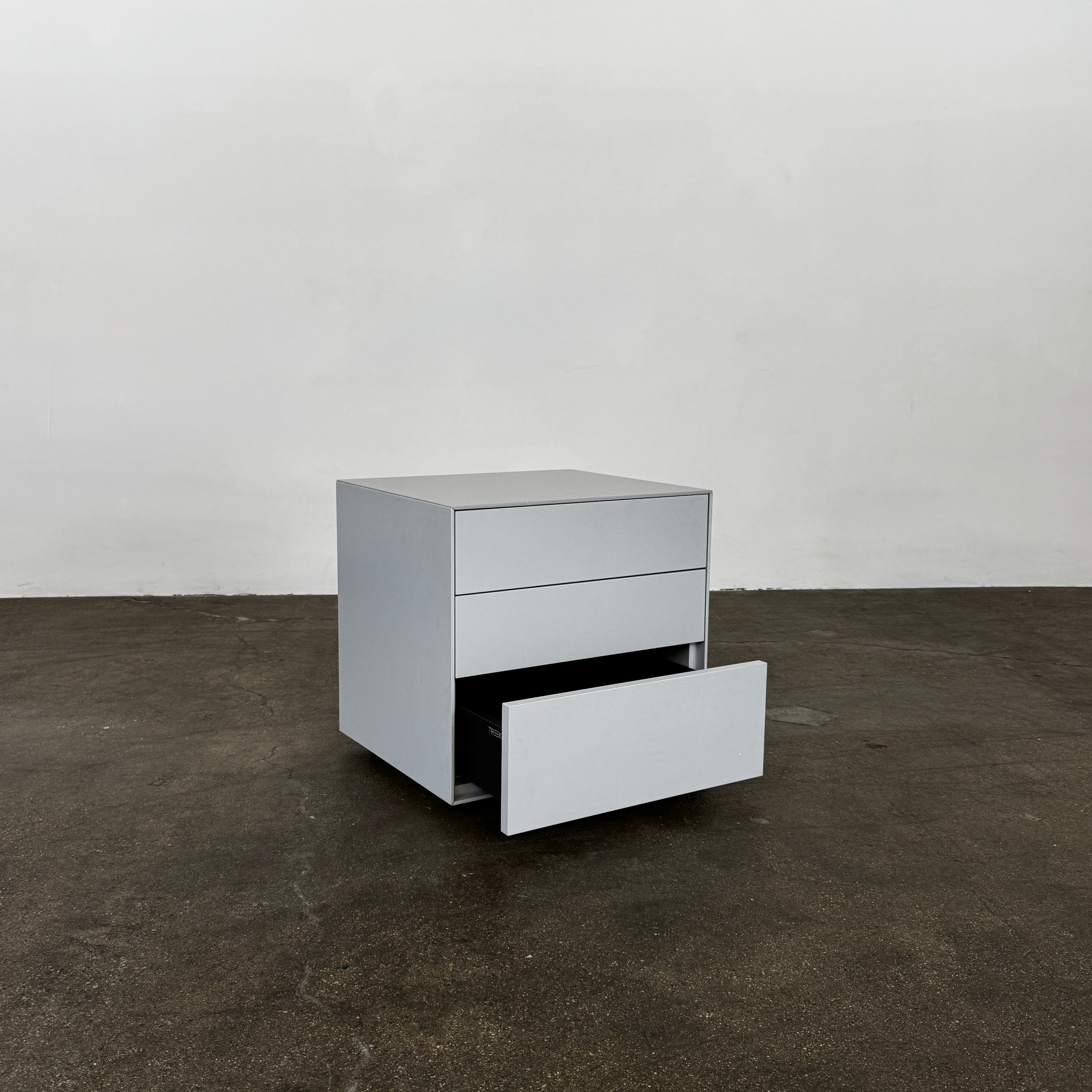 The Treku Lauki collection Side Table (2) by Treku, a gray rectangular side table with three drawers and a minimalist design, is shown against a plain white background.