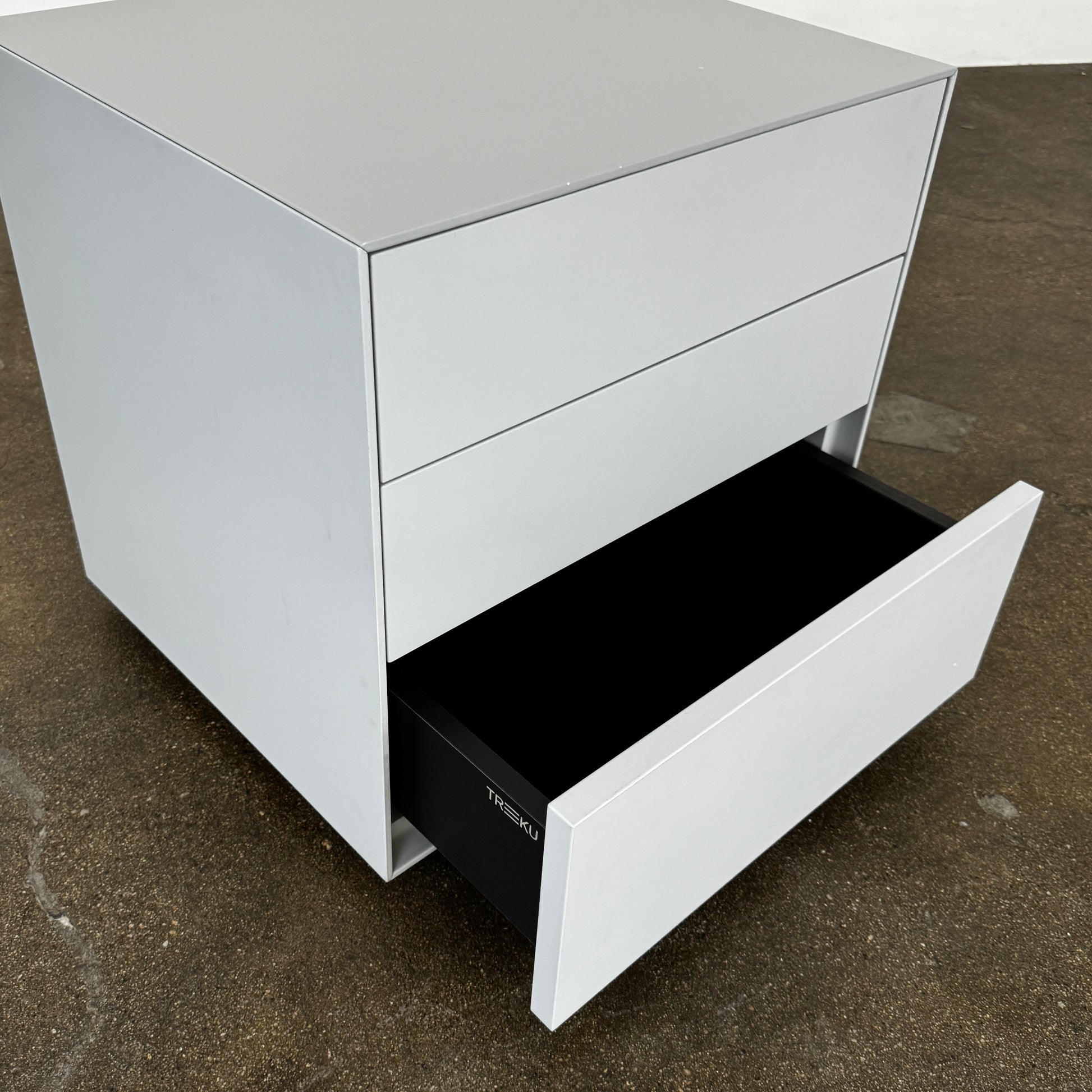 The Treku Lauki collection Side Table (2) by Treku, a gray rectangular side table with three drawers and a minimalist design, is shown against a plain white background.
