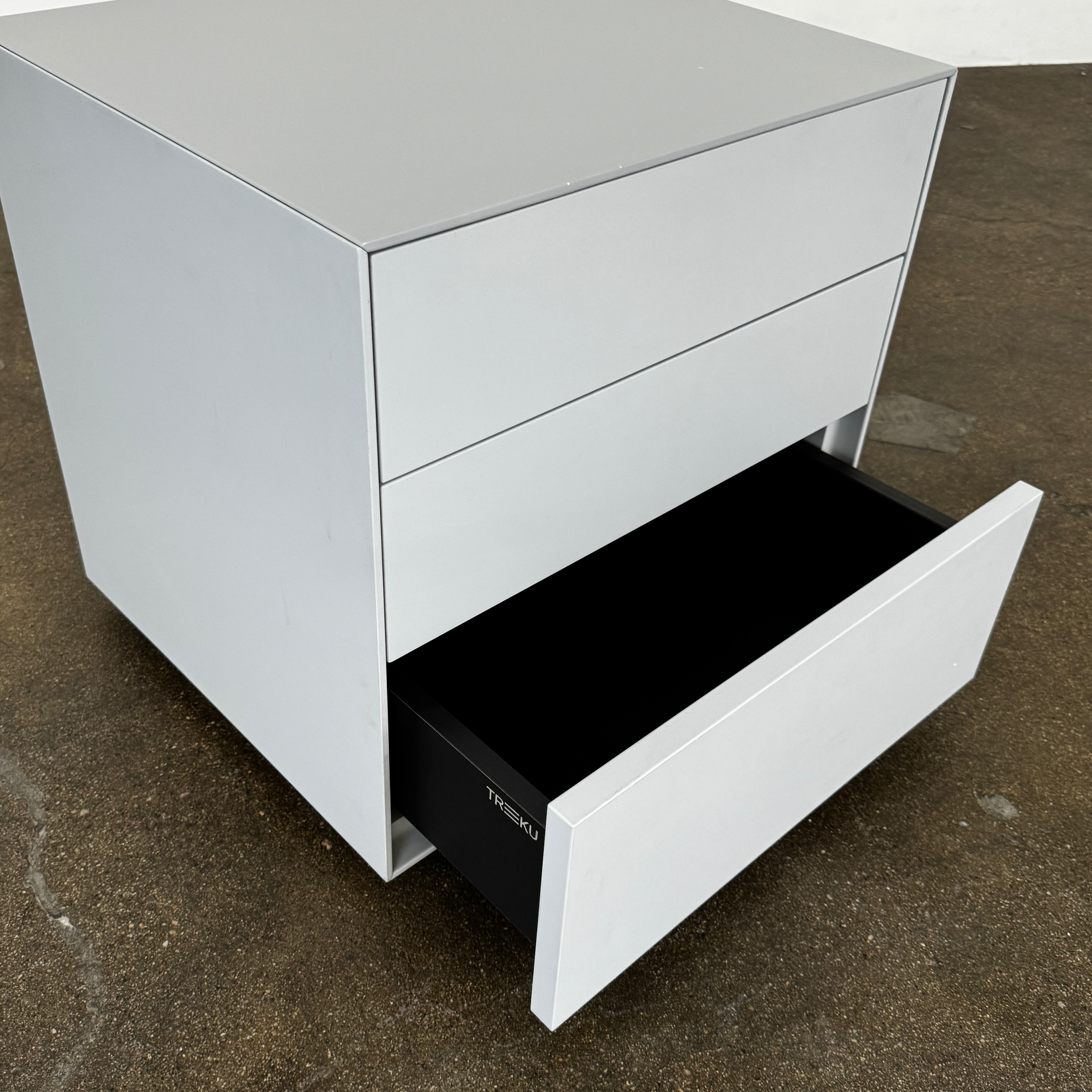 The Treku Lauki collection Side Table (2) by Treku, a gray rectangular side table with three drawers and a minimalist design, is shown against a plain white background.