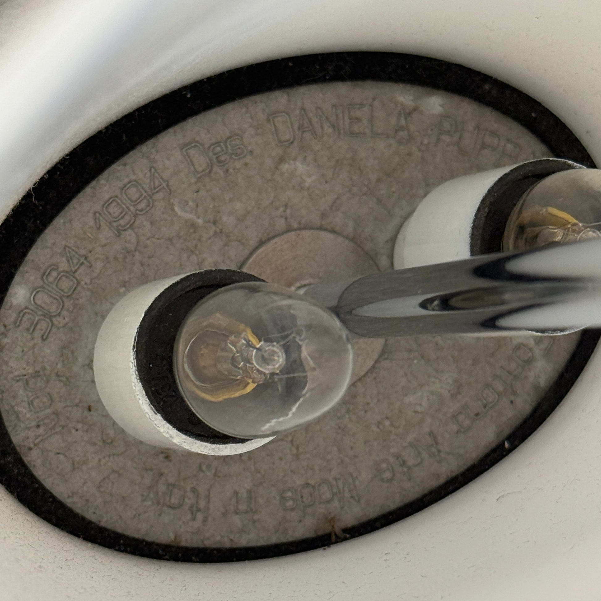 The Fontana Arte 3064 Table Light by Fontana Arte, echoing Daniela Puppa's designs, boasts a wide conical shade for a warm glow. It sits elegantly on a white surface against a plain backdrop, capturing the essence of postmodern art.