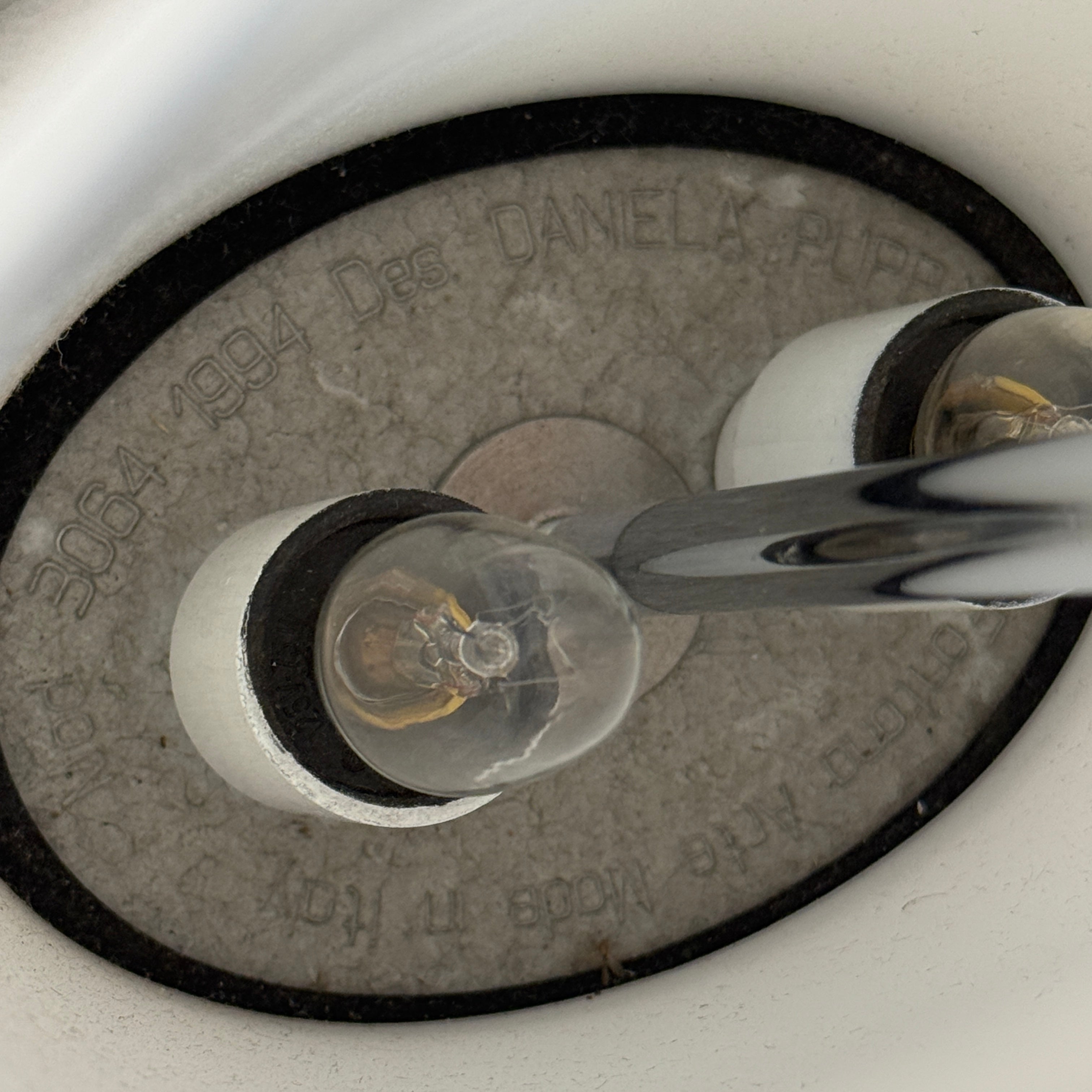 The Fontana Arte 3064 Table Light by Fontana Arte, echoing Daniela Puppa's designs, boasts a wide conical shade for a warm glow. It sits elegantly on a white surface against a plain backdrop, capturing the essence of postmodern art.