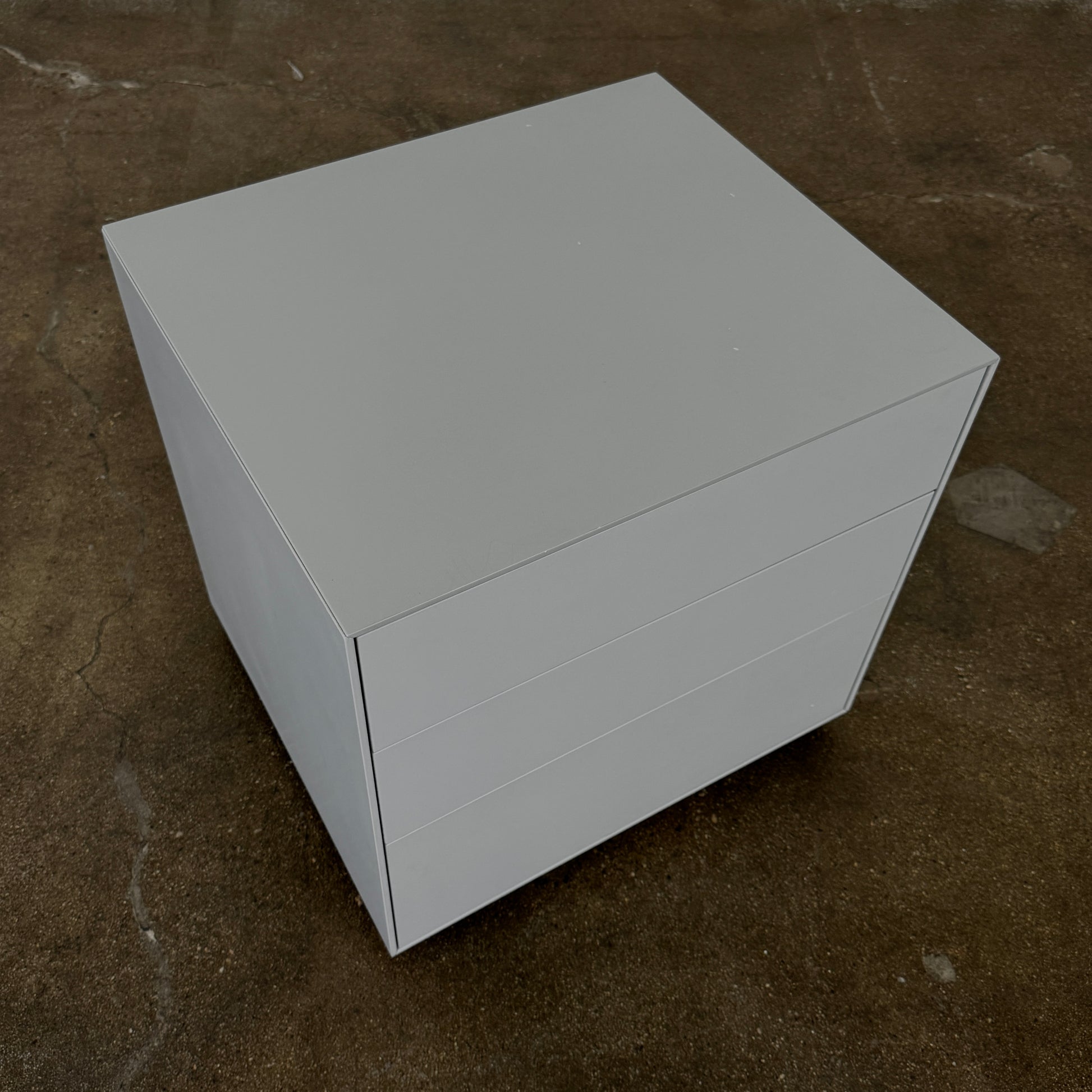 The Treku Lauki collection Side Table (2) by Treku, a gray rectangular side table with three drawers and a minimalist design, is shown against a plain white background.
