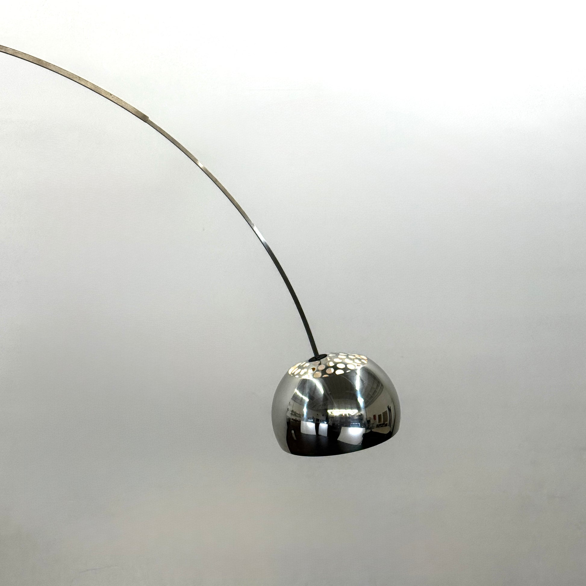 The Flos Arco Floor Lamp by Flos features a curved metal arm, dome-shaped metallic shade, and a rectangular marble base, inspired by the iconic original design.