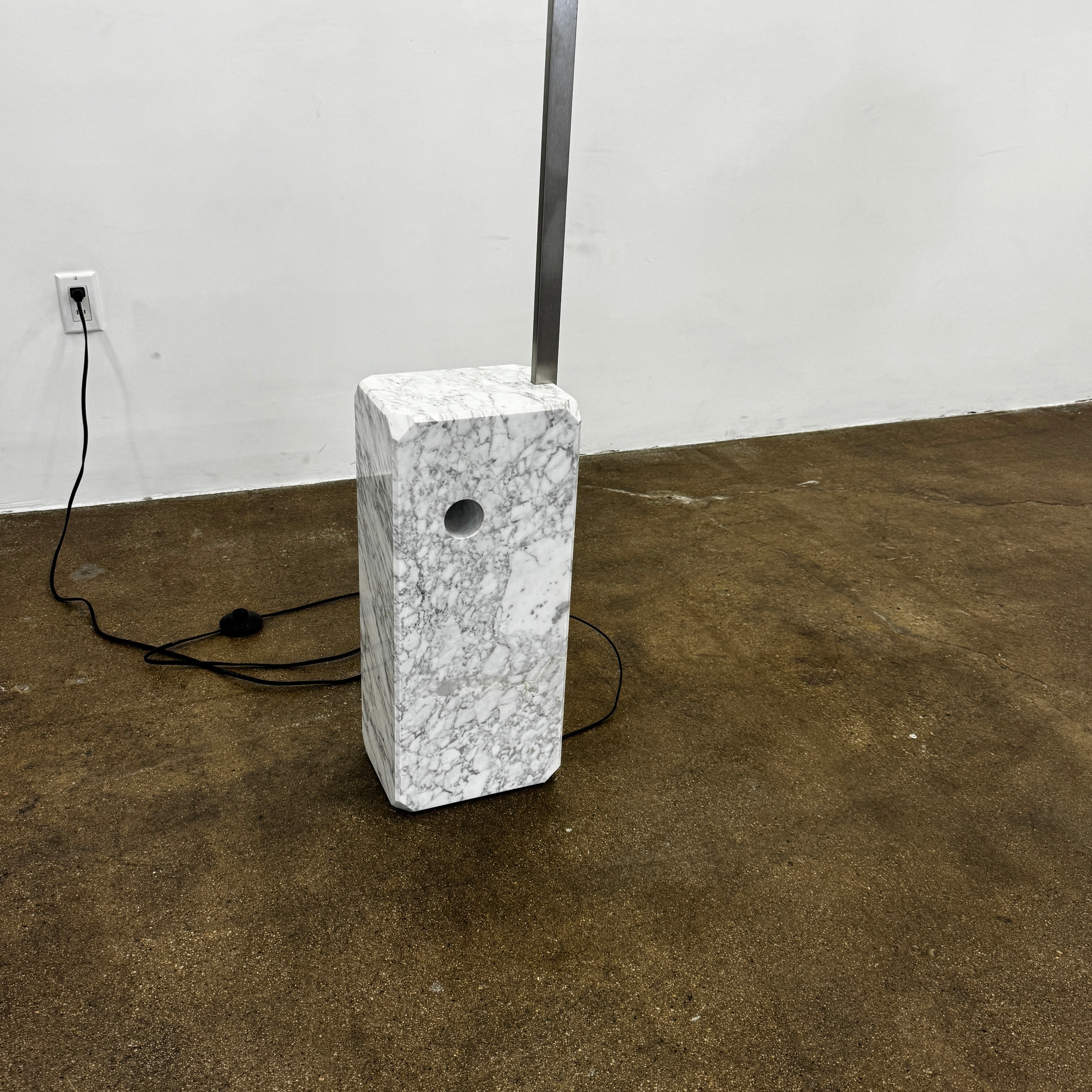 The Flos Arco Floor Lamp by Flos features a curved metal arm, dome-shaped metallic shade, and a rectangular marble base, inspired by the iconic original design.