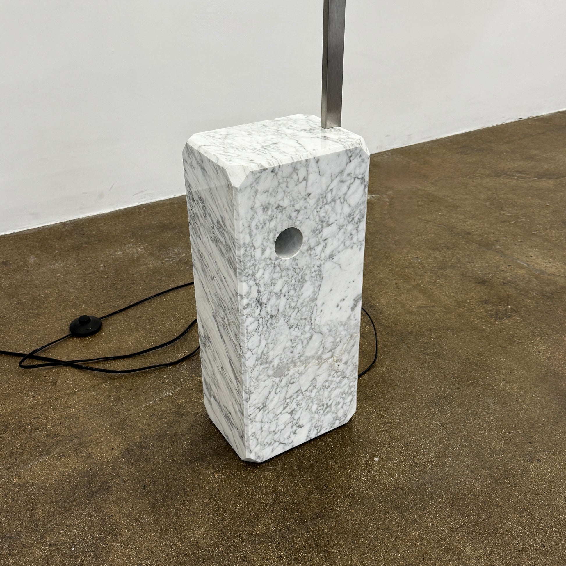 The Flos Arco Floor Lamp by Flos features a curved metal arm, dome-shaped metallic shade, and a rectangular marble base, inspired by the iconic original design.