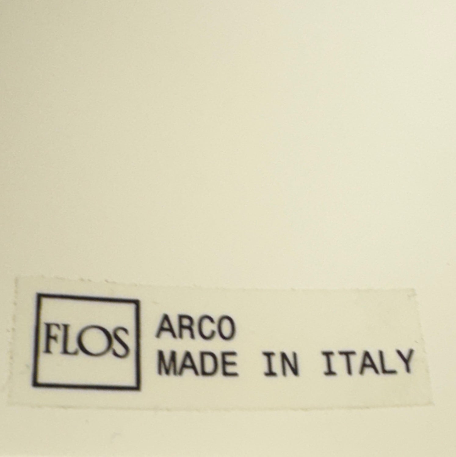 The Flos Arco Floor Lamp by Flos features a curved metal arm, dome-shaped metallic shade, and a rectangular marble base, inspired by the iconic original design.