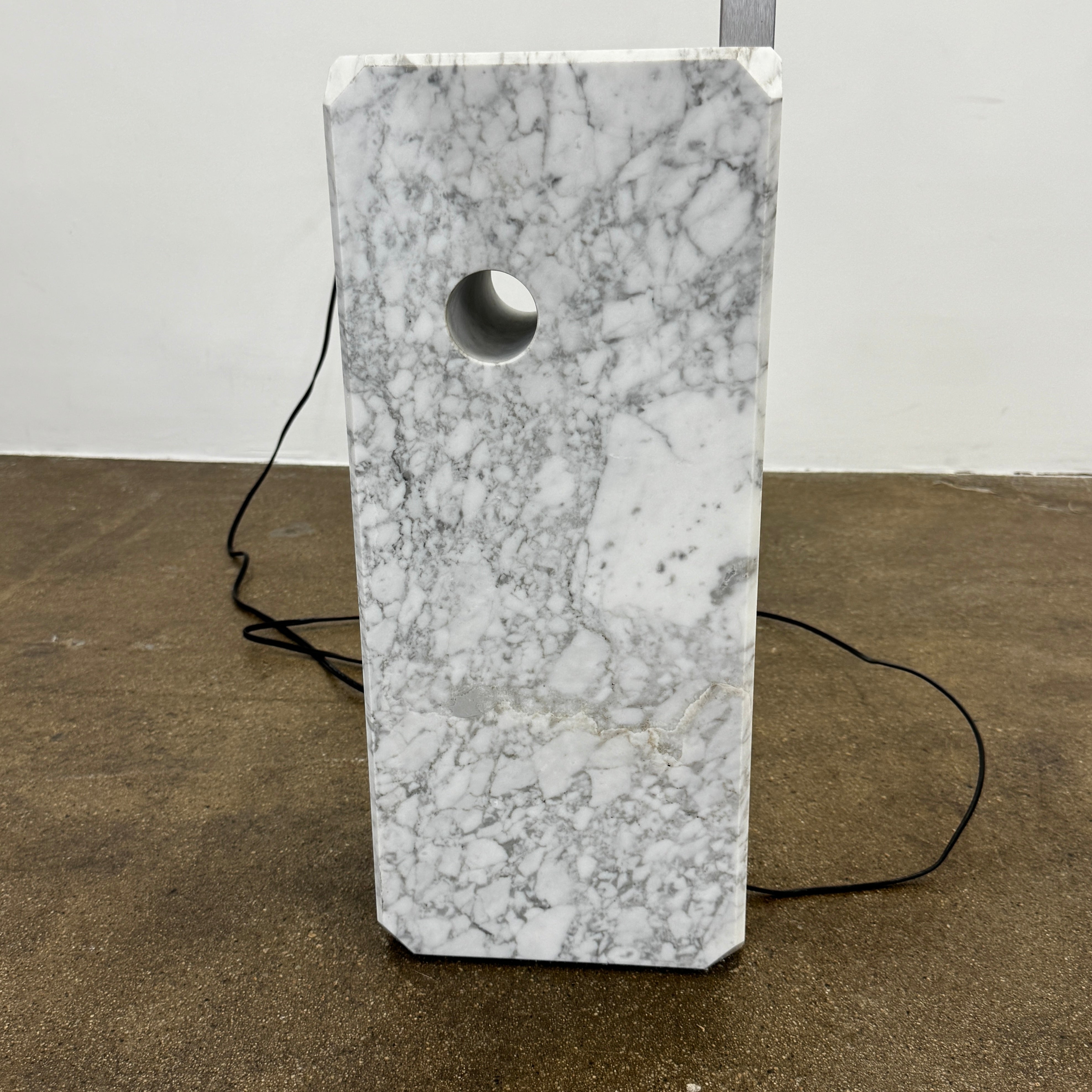 The Flos Arco Floor Lamp by Flos features a curved metal arm, dome-shaped metallic shade, and a rectangular marble base, inspired by the iconic original design.