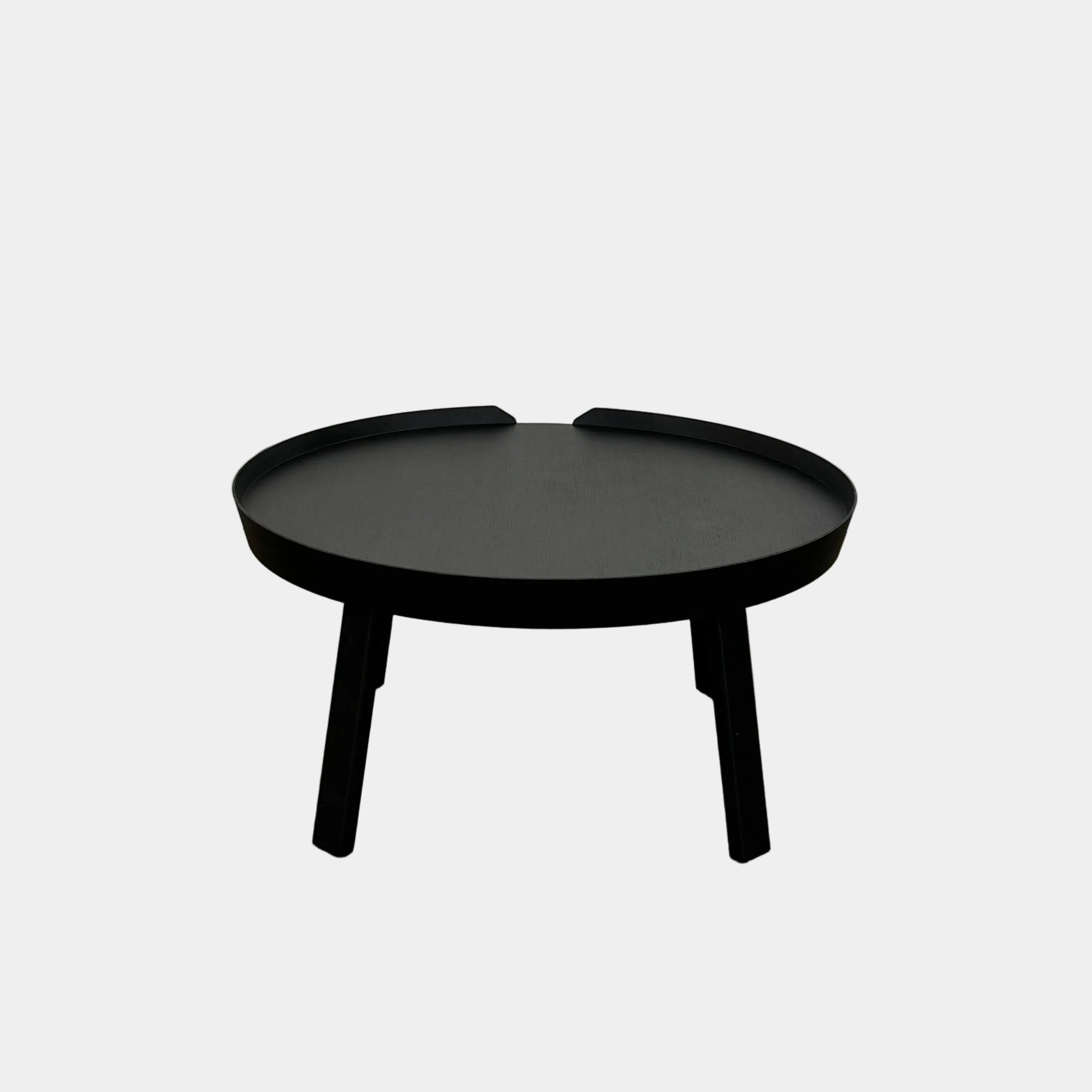 The Muuto Around Coffee Table by Muuto is a round, black wooden table with three legs and Scandinavian design, displayed against a plain light background.