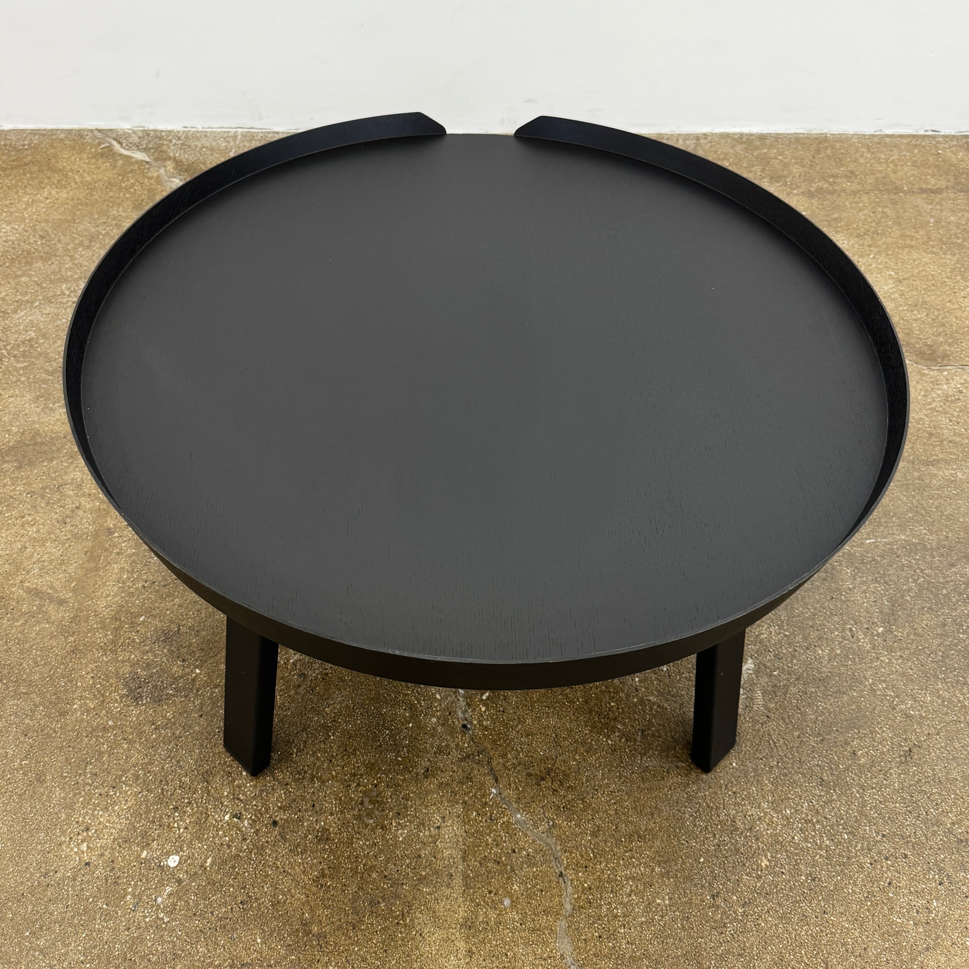 The Muuto Around Coffee Table by Muuto is a round, black wooden table with three legs and Scandinavian design, displayed against a plain light background.
