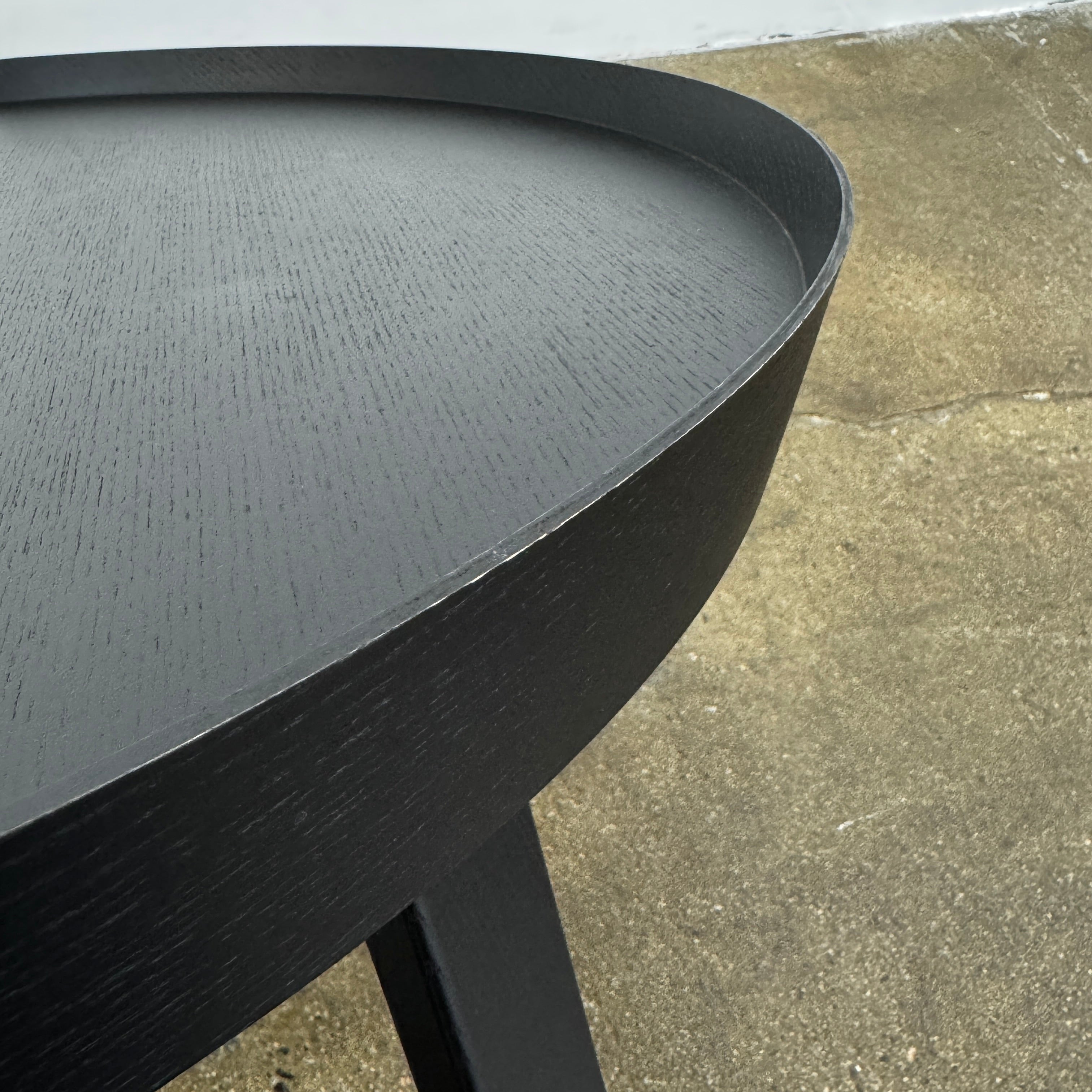 The Muuto Around Coffee Table by Muuto is a round, black wooden table with three legs and Scandinavian design, displayed against a plain light background.