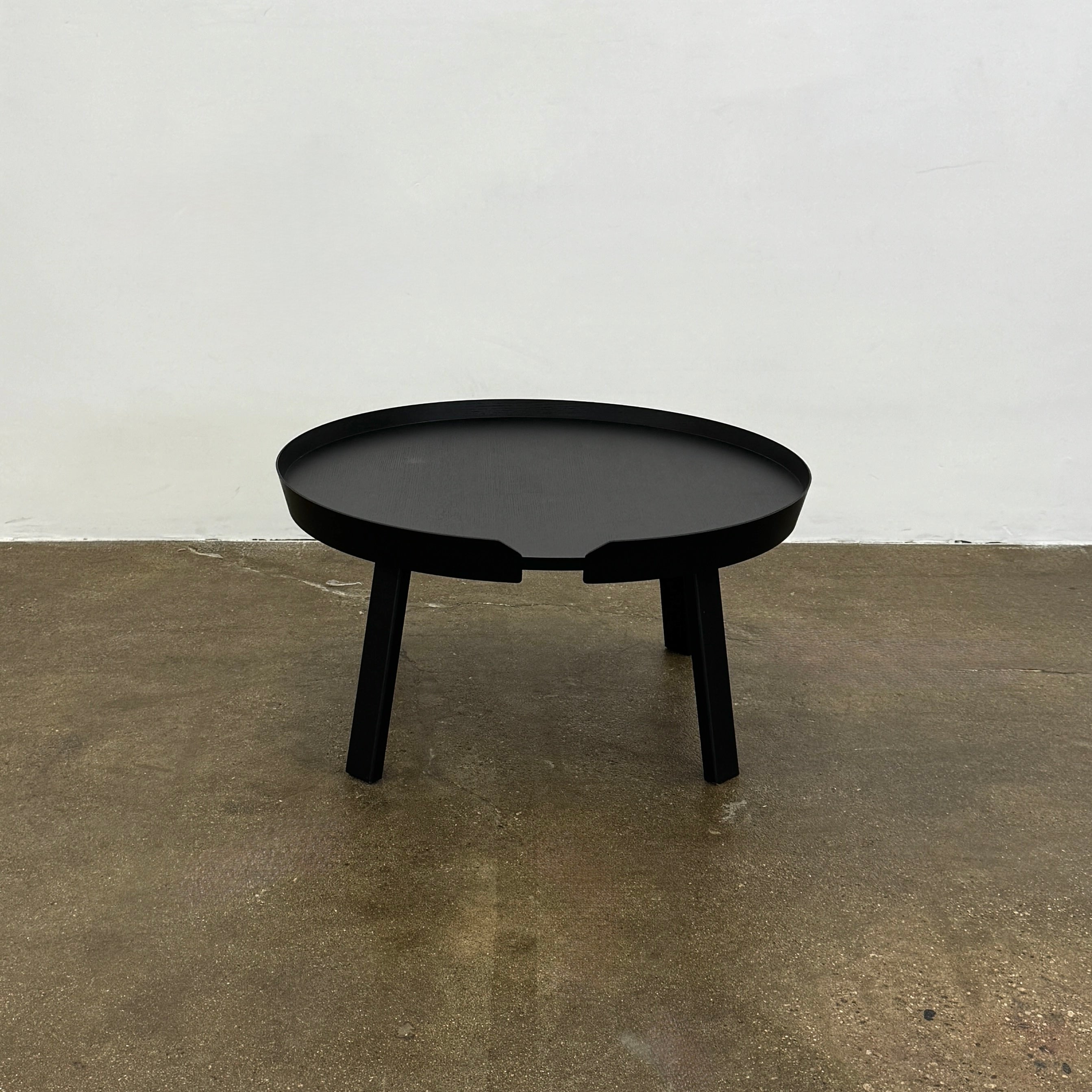 The Muuto Around Coffee Table by Muuto is a round, black wooden table with three legs and Scandinavian design, displayed against a plain light background.
