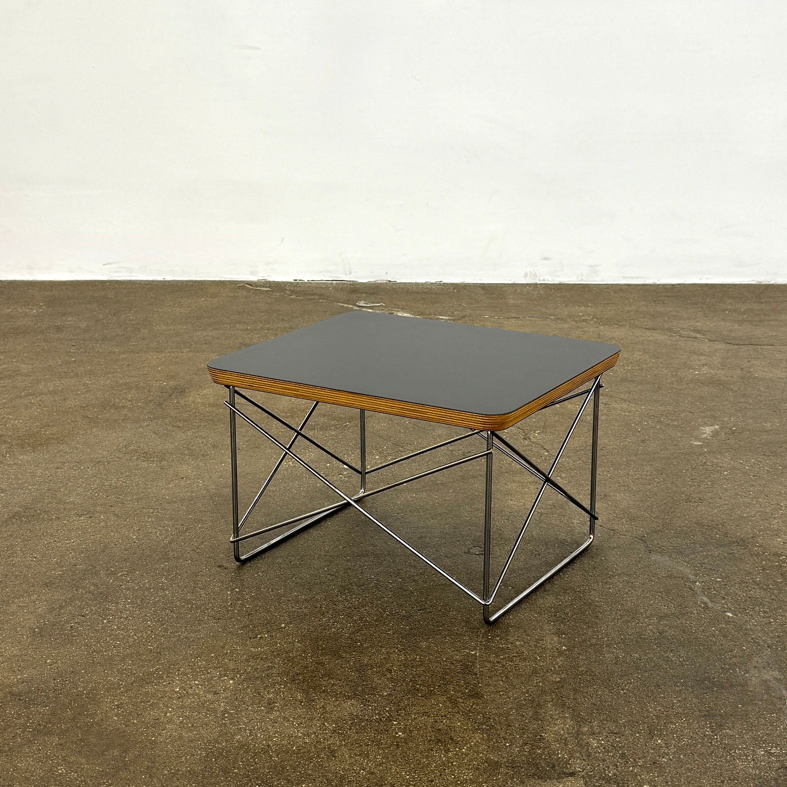 Two Herman Miller Eames Wire Base Low Tables are set side by side on a light wood floor in a bright, minimalist room, showcasing the iconic design and craftsmanship of Herman Miller.