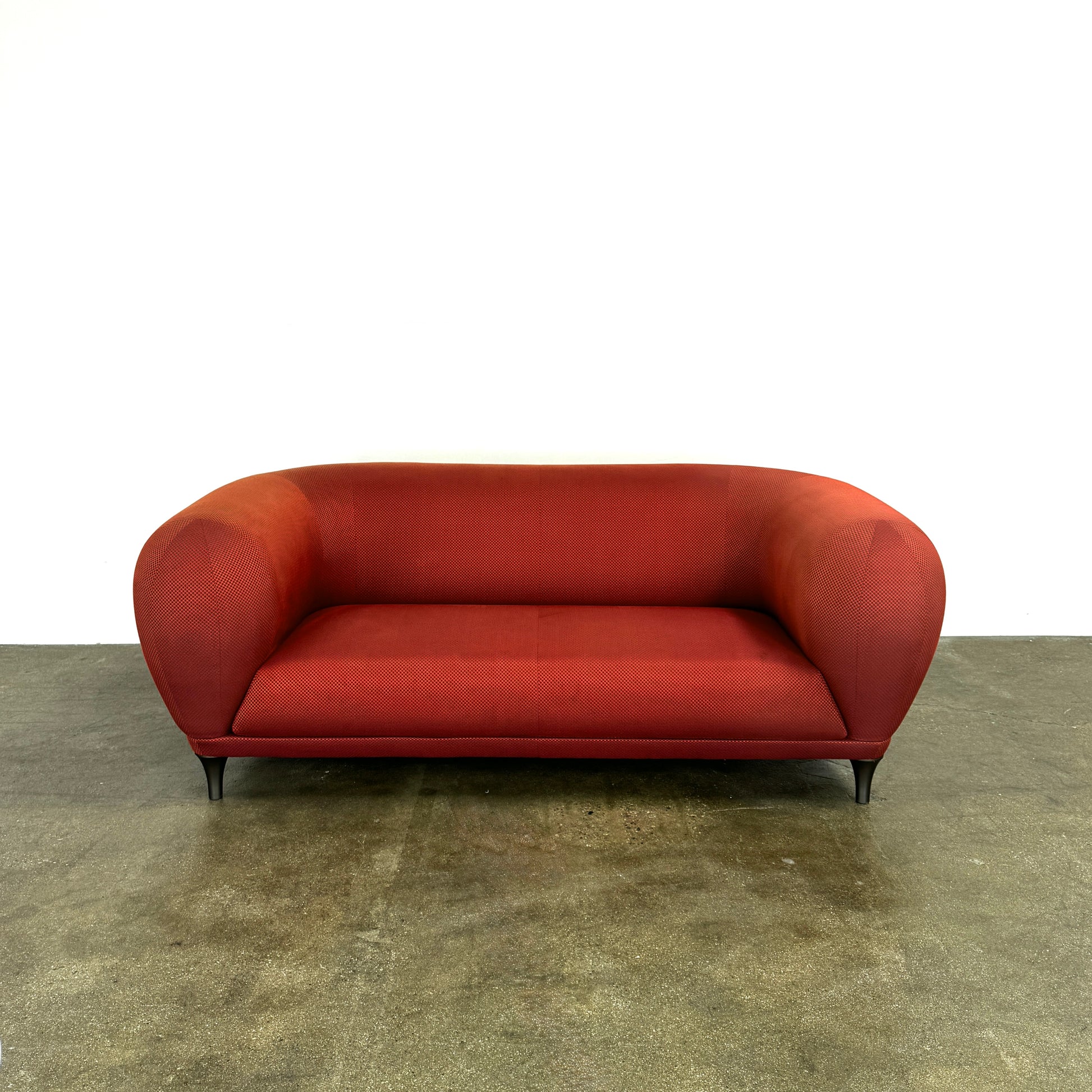 The Roche Bobois Montgolfiere Love seat is a modern, red 2-seat sofa with curved arms and dark wooden legs by Roche Bobois, shown against a plain background.