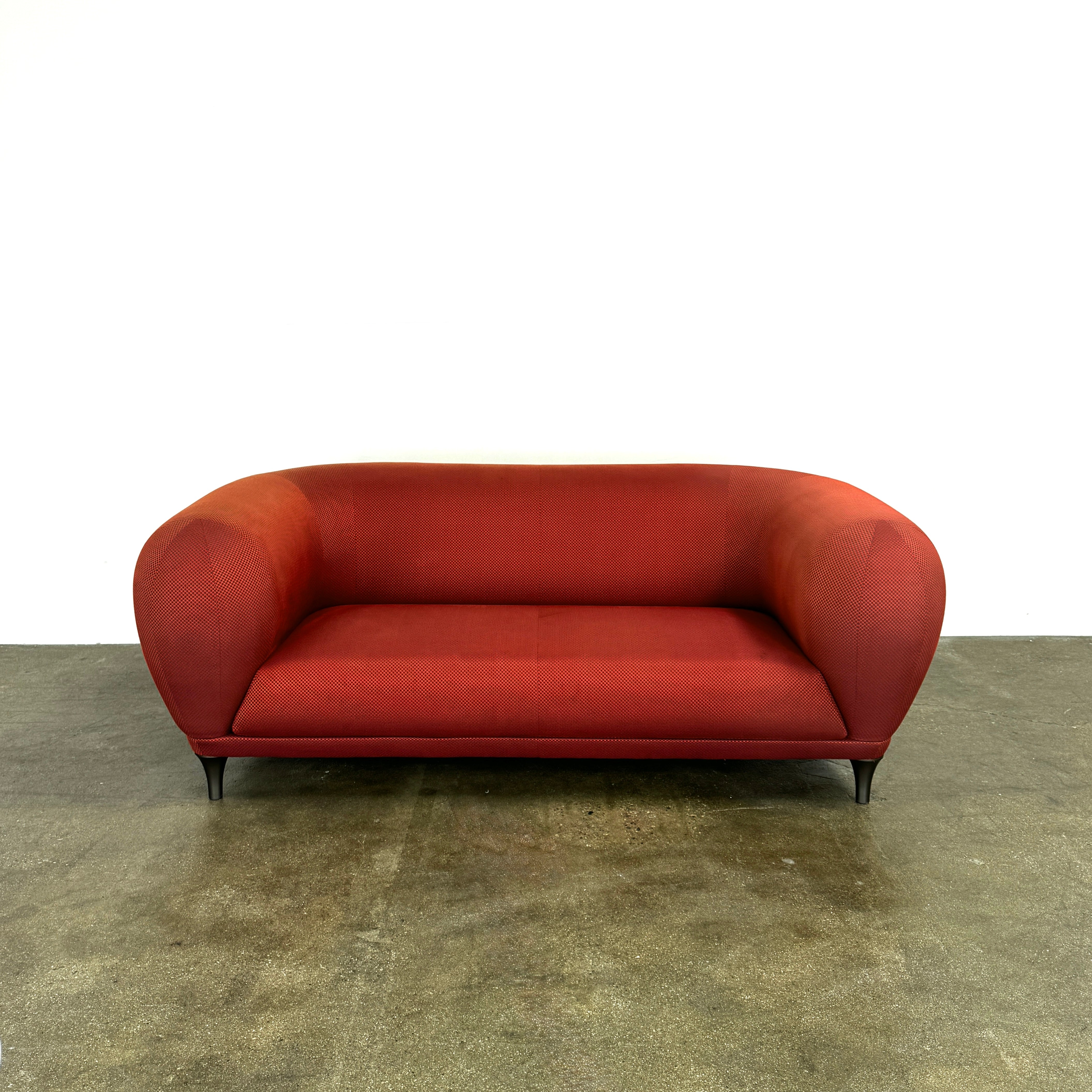 The Roche Bobois Montgolfiere Love seat is a modern, red 2-seat sofa with curved arms and dark wooden legs by Roche Bobois, shown against a plain background.
