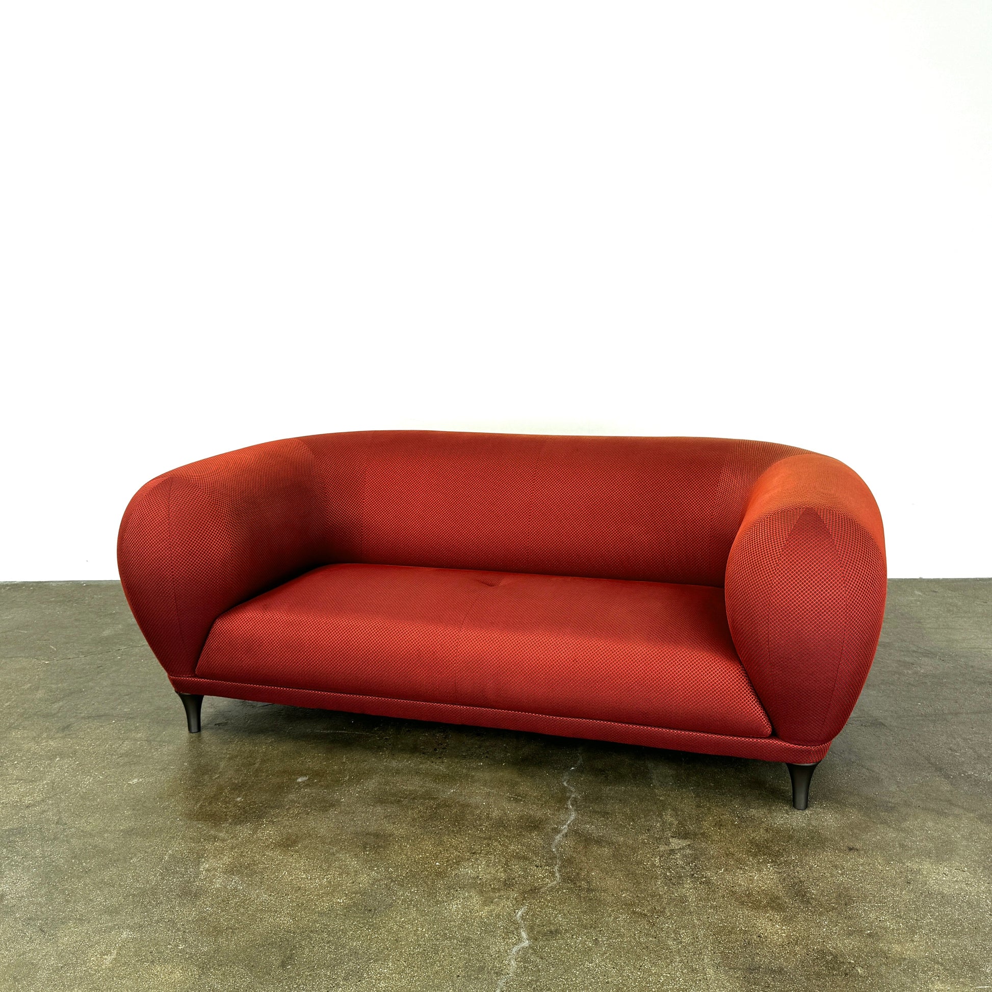 The Roche Bobois Montgolfiere Love seat is a modern, red 2-seat sofa with curved arms and dark wooden legs by Roche Bobois, shown against a plain background.