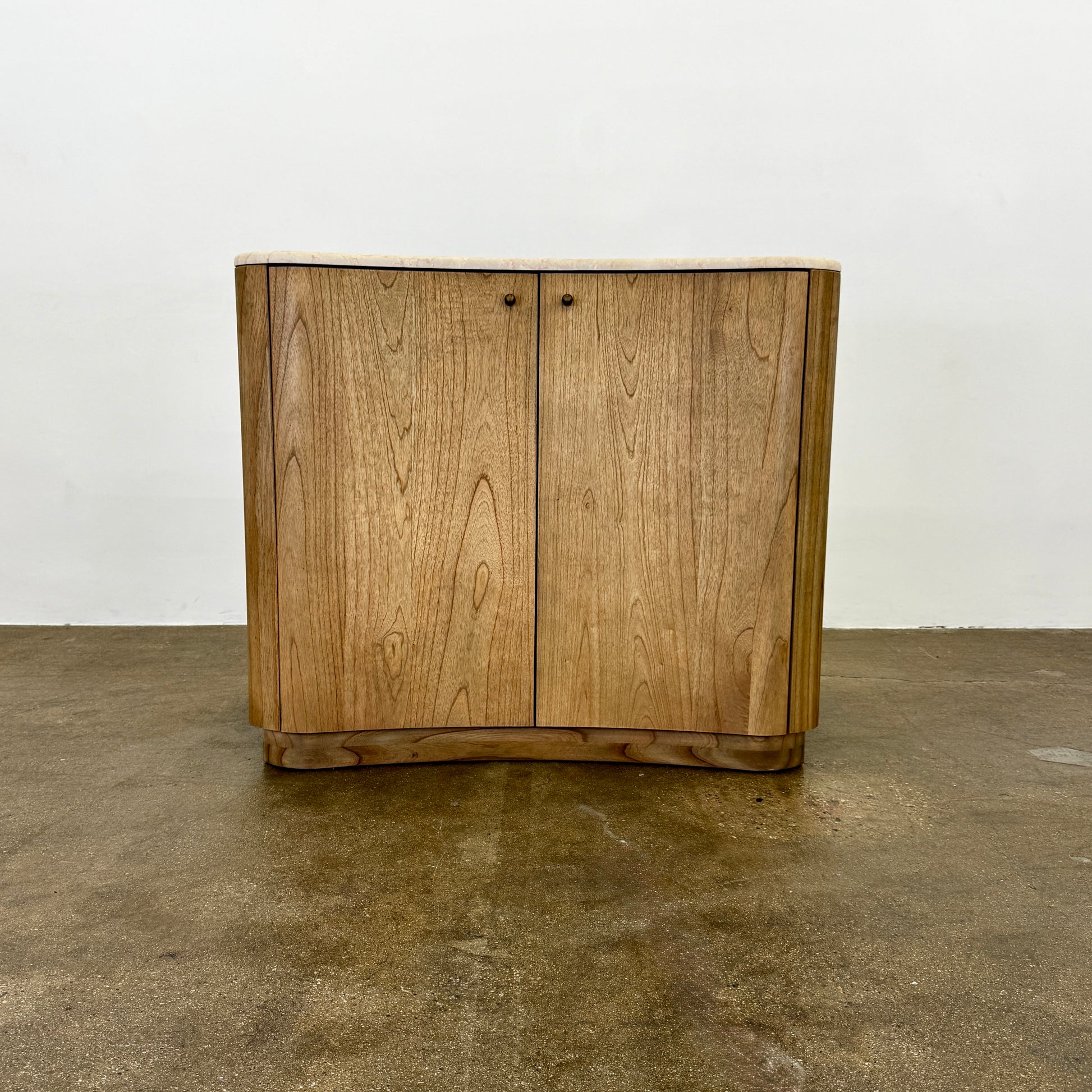 The Boa Small Cabinet by Fourhands features two doors, a gently curved front, light natural wood finish, and round handles, bringing contemporary style to any space.