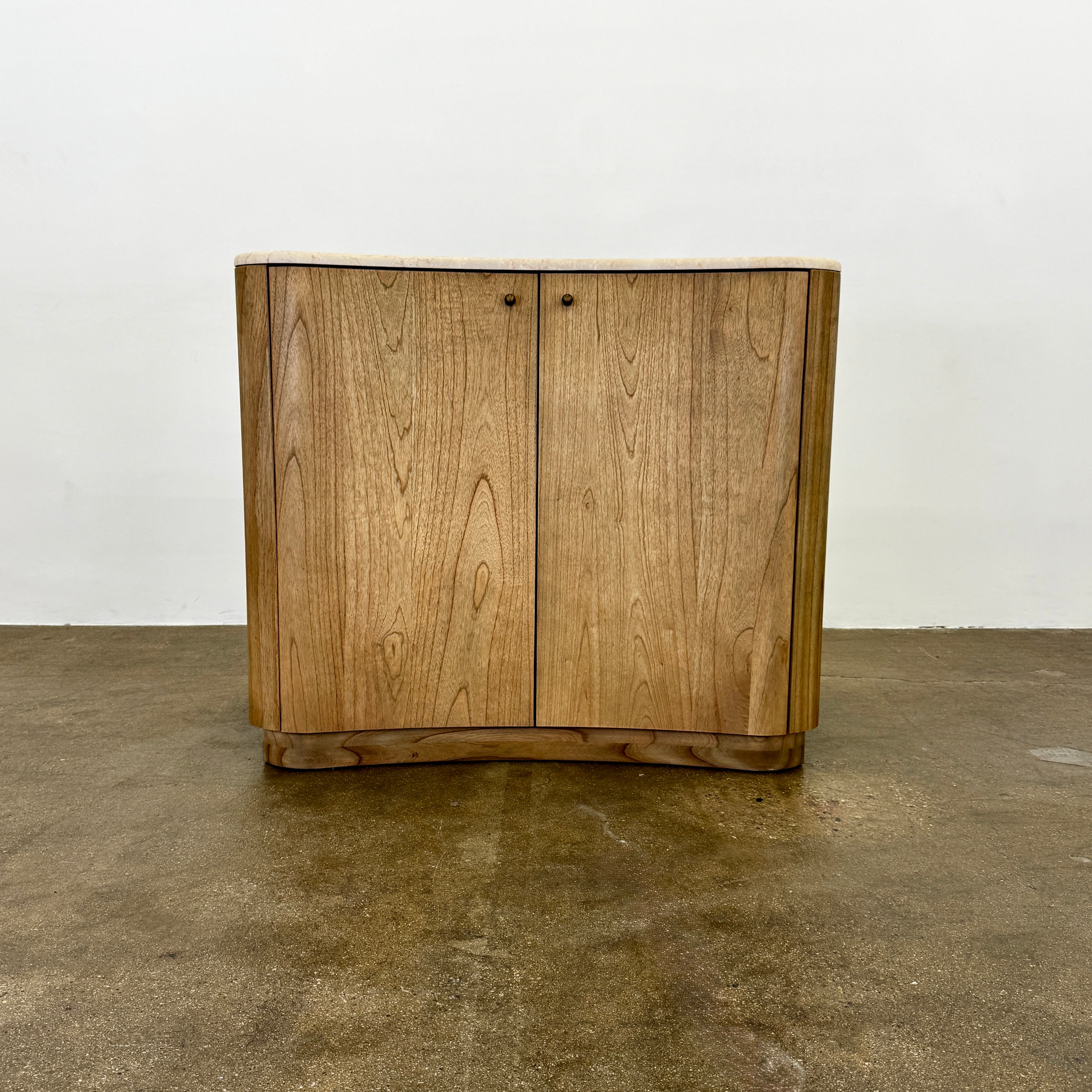 The Boa Small Cabinet by Fourhands features two doors, a gently curved front, light natural wood finish, and round handles, bringing contemporary style to any space.