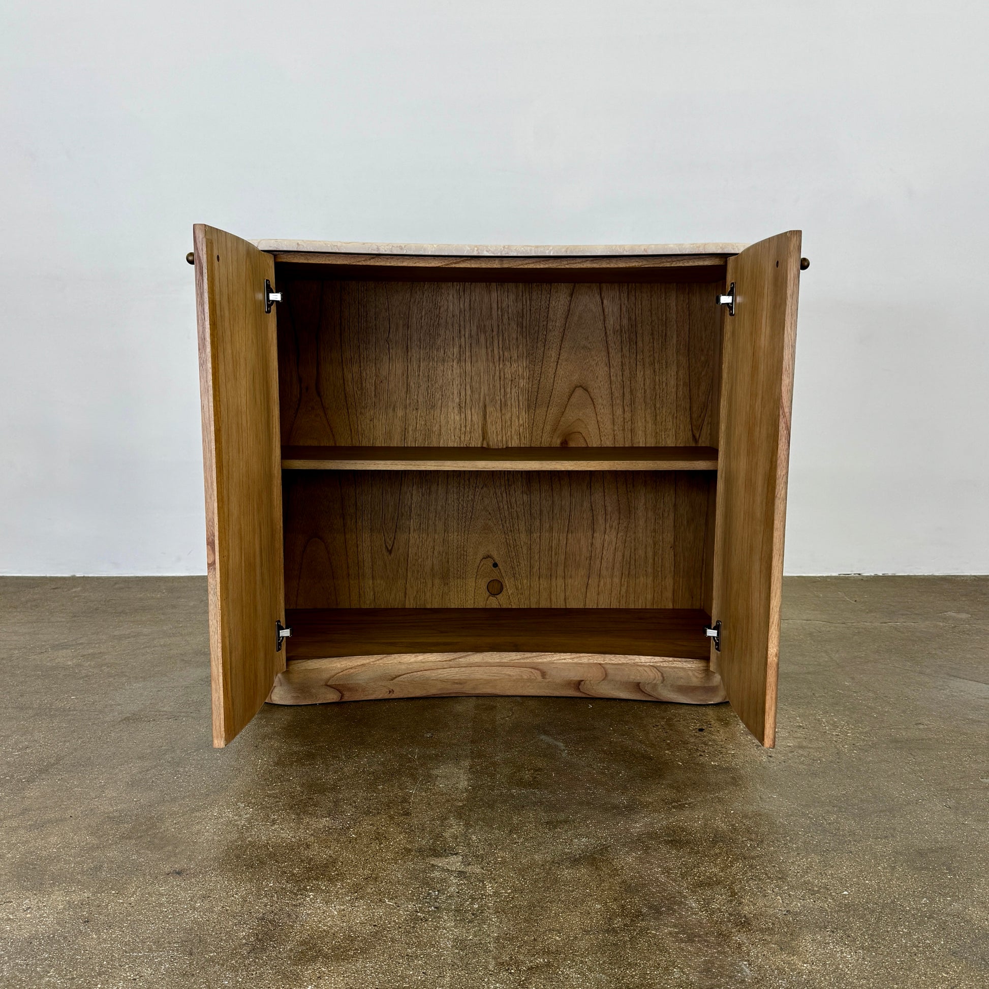 The Boa Small Cabinet by Fourhands features two doors, a gently curved front, light natural wood finish, and round handles, bringing contemporary style to any space.