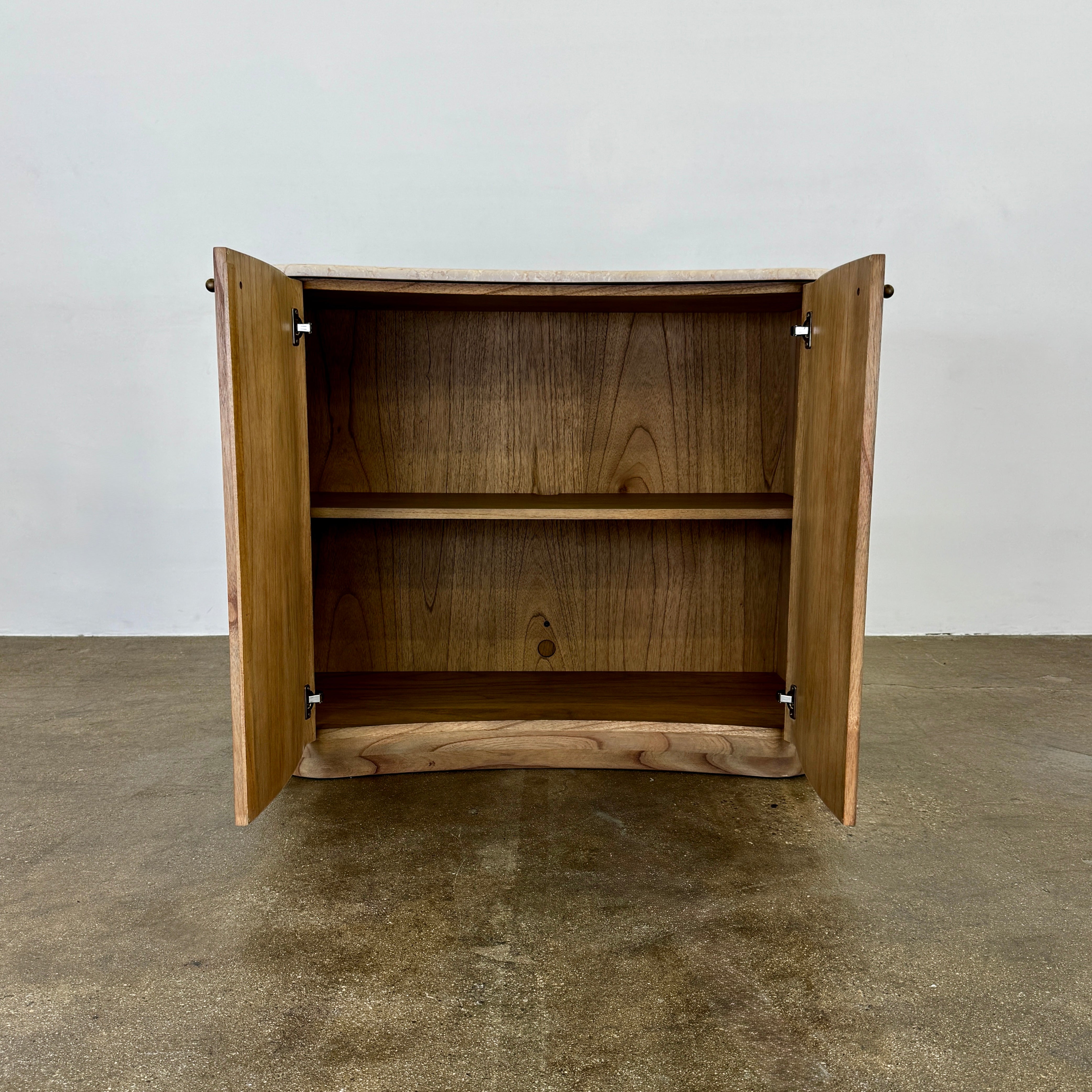 The Boa Small Cabinet by Fourhands features two doors, a gently curved front, light natural wood finish, and round handles, bringing contemporary style to any space.