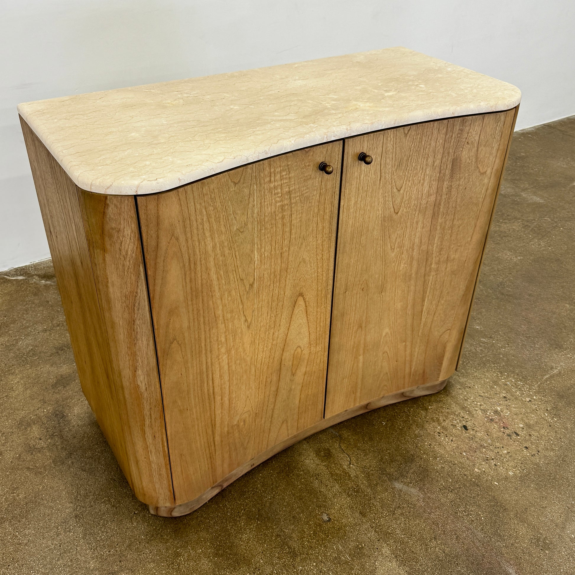 The Boa Small Cabinet by Fourhands features two doors, a gently curved front, light natural wood finish, and round handles, bringing contemporary style to any space.