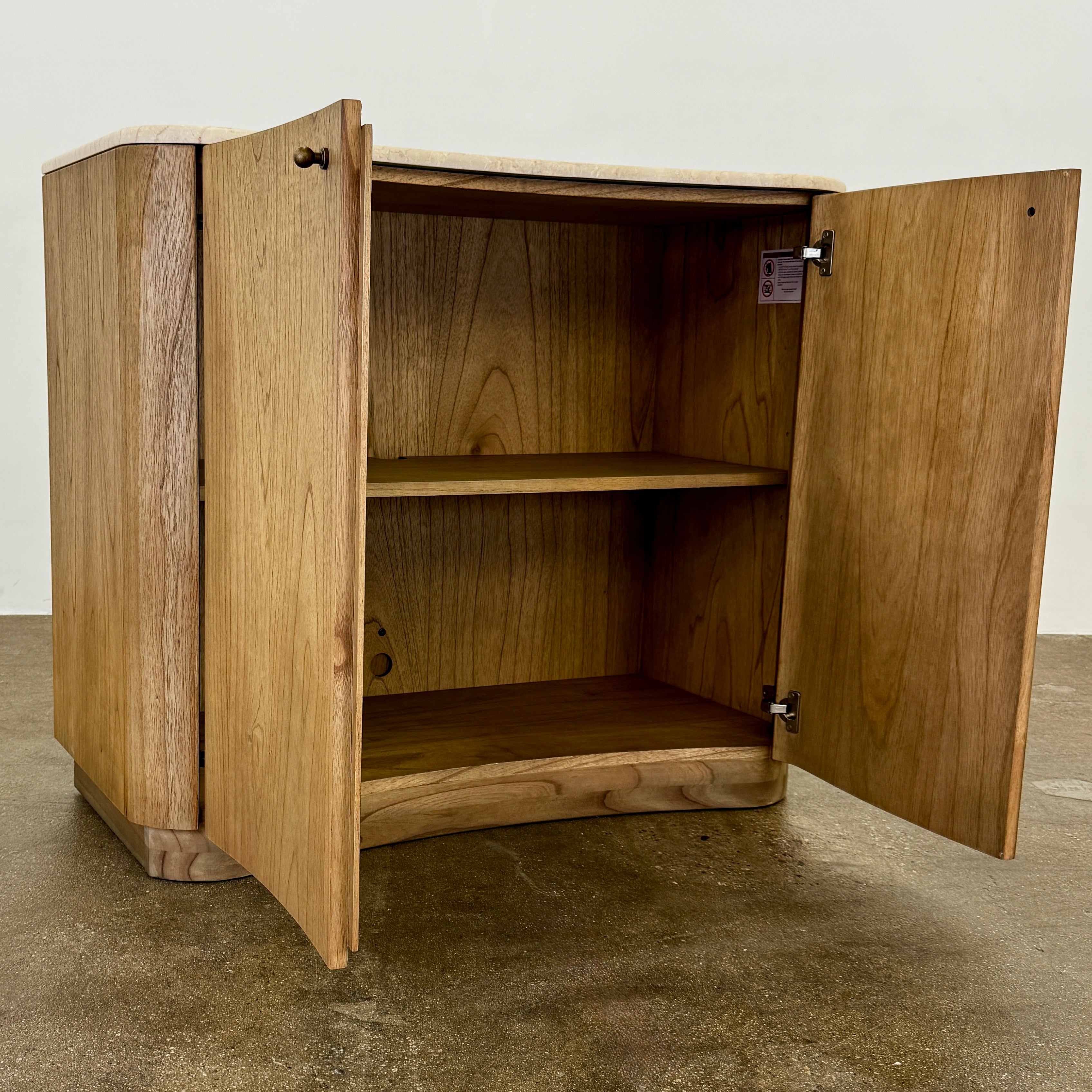 The Boa Small Cabinet by Fourhands features two doors, a gently curved front, light natural wood finish, and round handles, bringing contemporary style to any space.