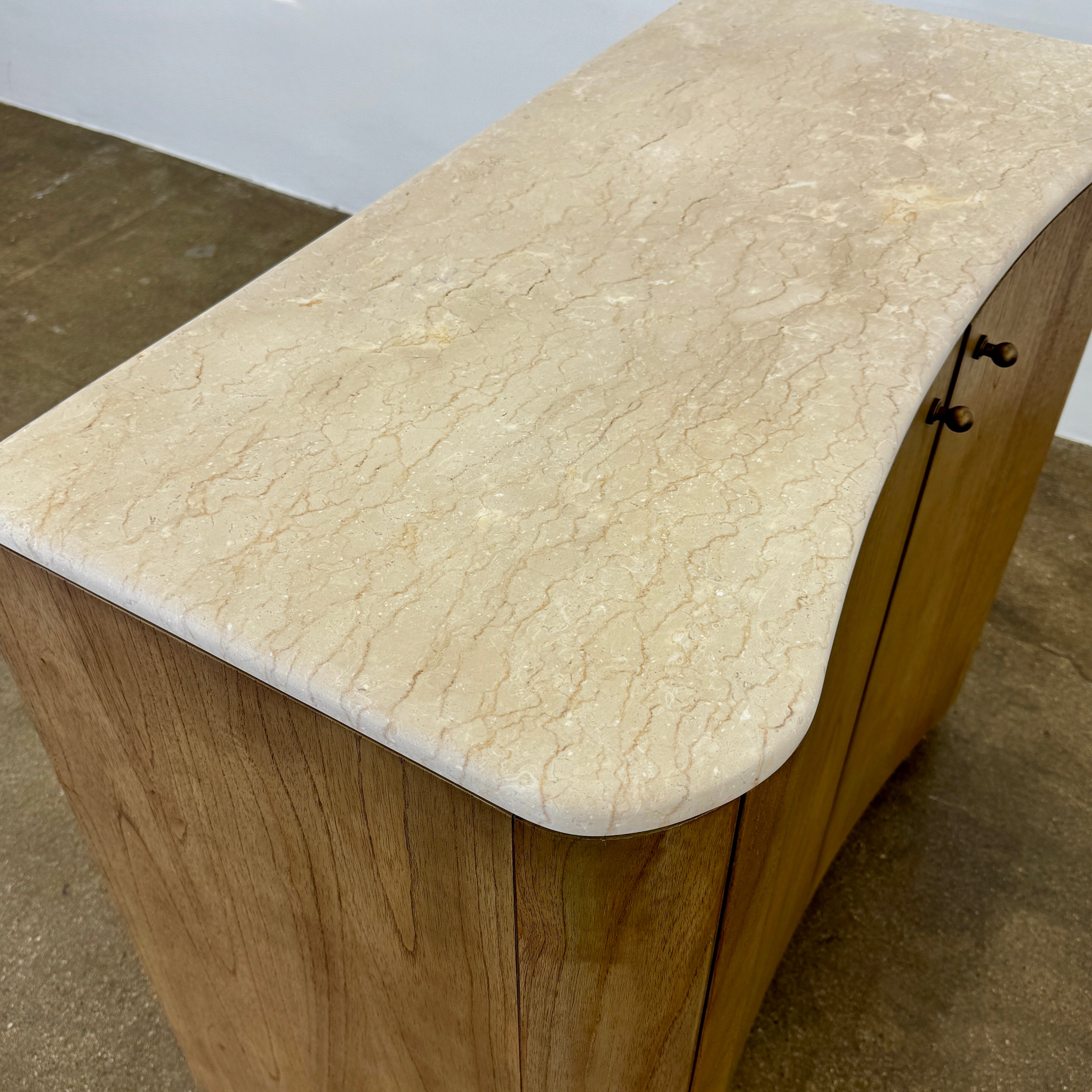 The Boa Small Cabinet by Fourhands features two doors, a gently curved front, light natural wood finish, and round handles, bringing contemporary style to any space.