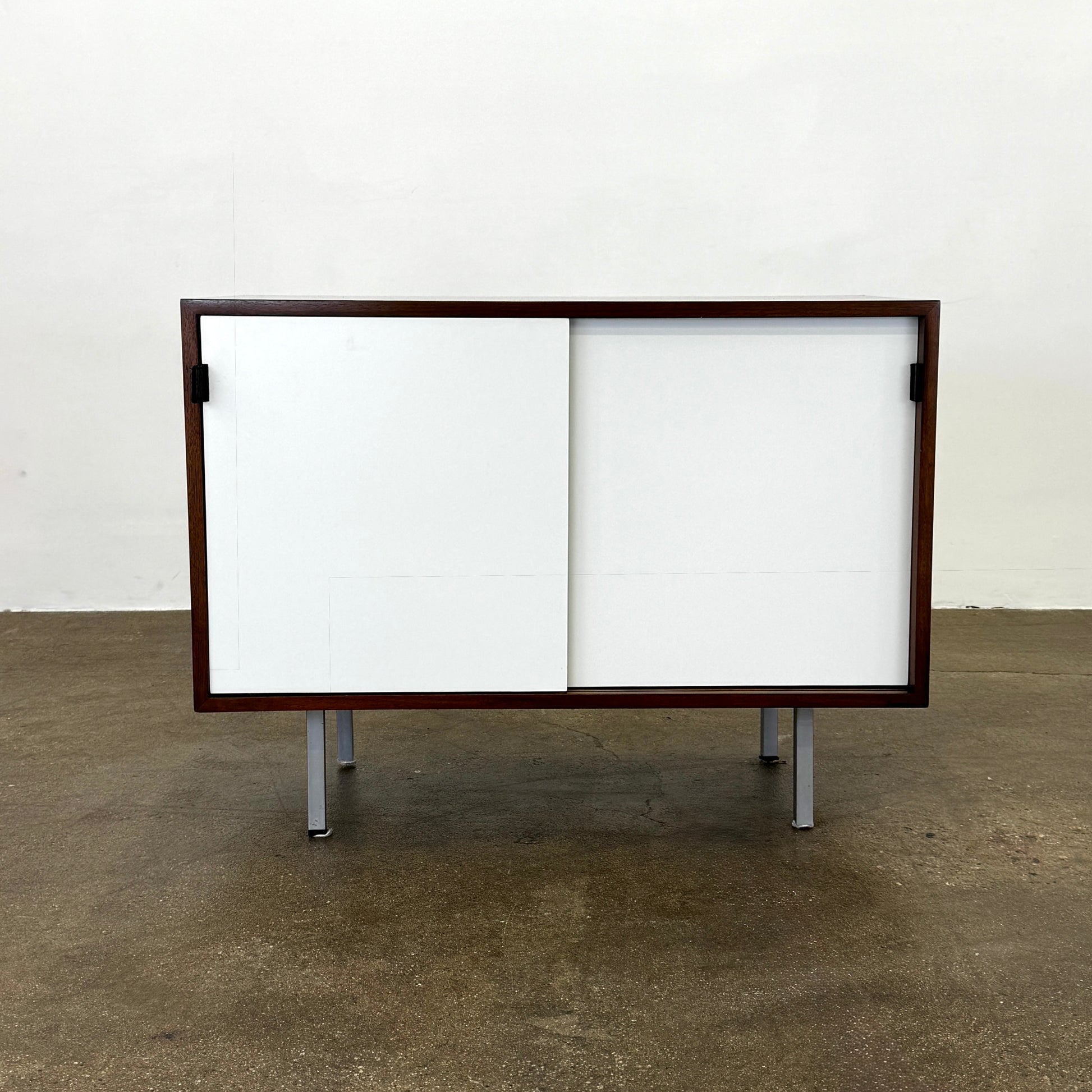 The Knoll Vintage Florence Knoll Office Storage features a dark wood frame, white sliding doors, and metal legs—perfect as a stylish credenza or office storage against a plain white wall.