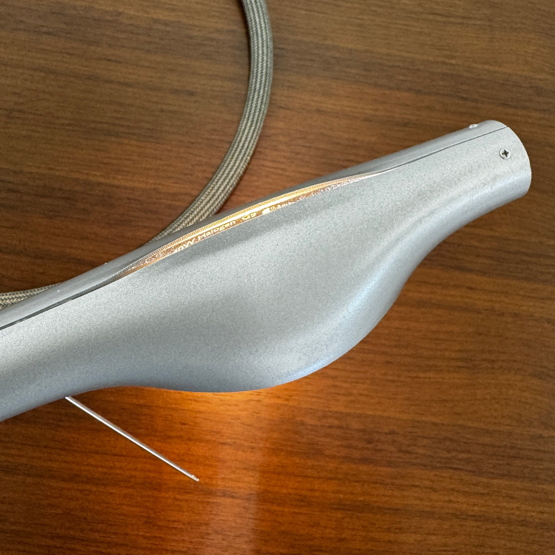 The Ingo Maurer Metall T. Cooper Task Light features a flexible metal braided hose with a metallic nozzle on one end and exposed wires on the other, coiled on a plain white background—evoking collectible German designer lighting.