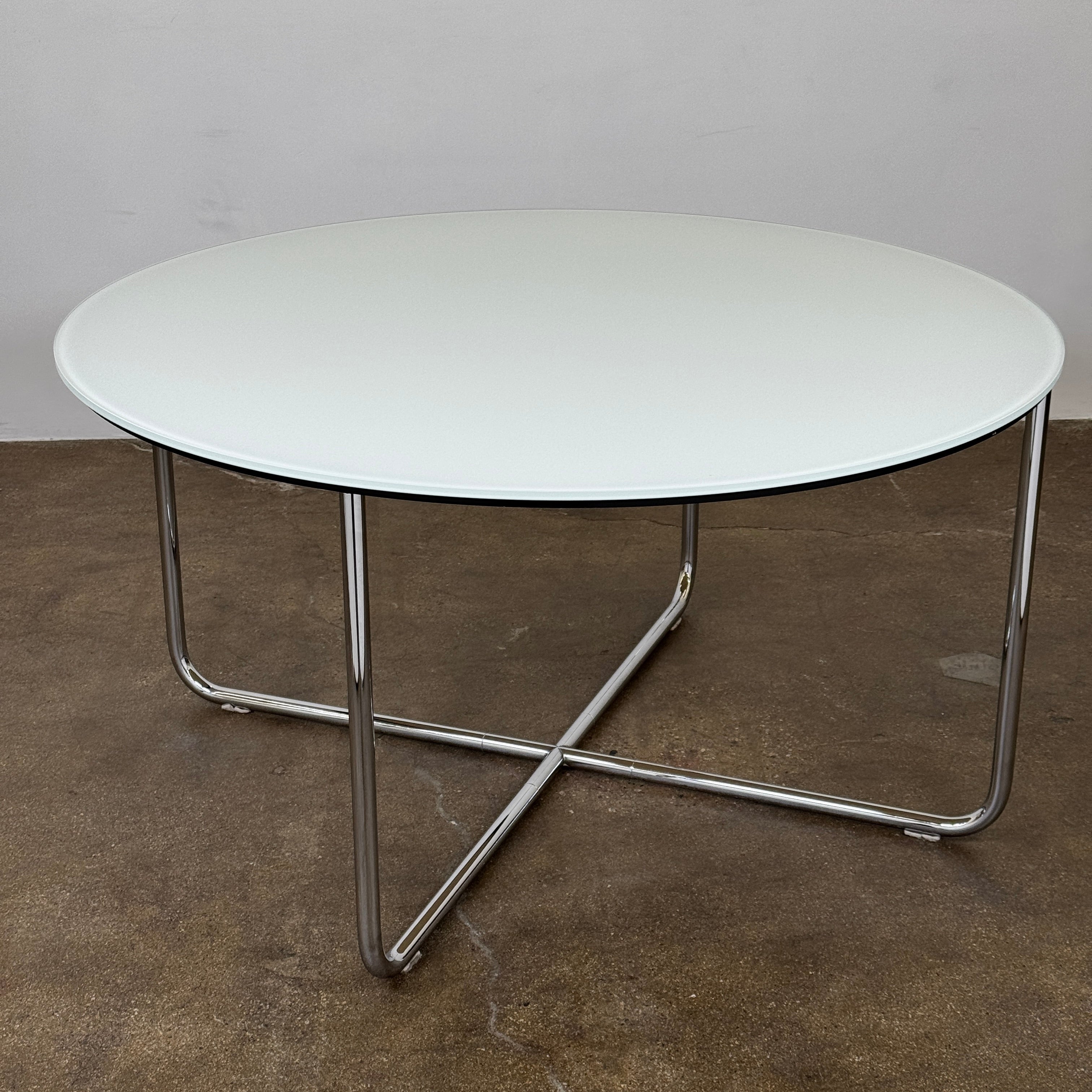The Minotti Louis Round Dining Table features a white top and a modern metal base with three intersecting legs, reflecting Minotti’s signature style.