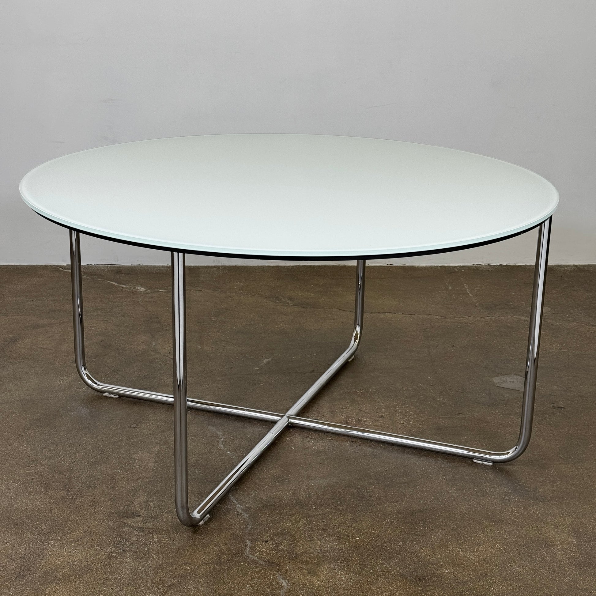 The Minotti Louis Round Dining Table features a white top and a modern metal base with three intersecting legs, reflecting Minotti’s signature style.