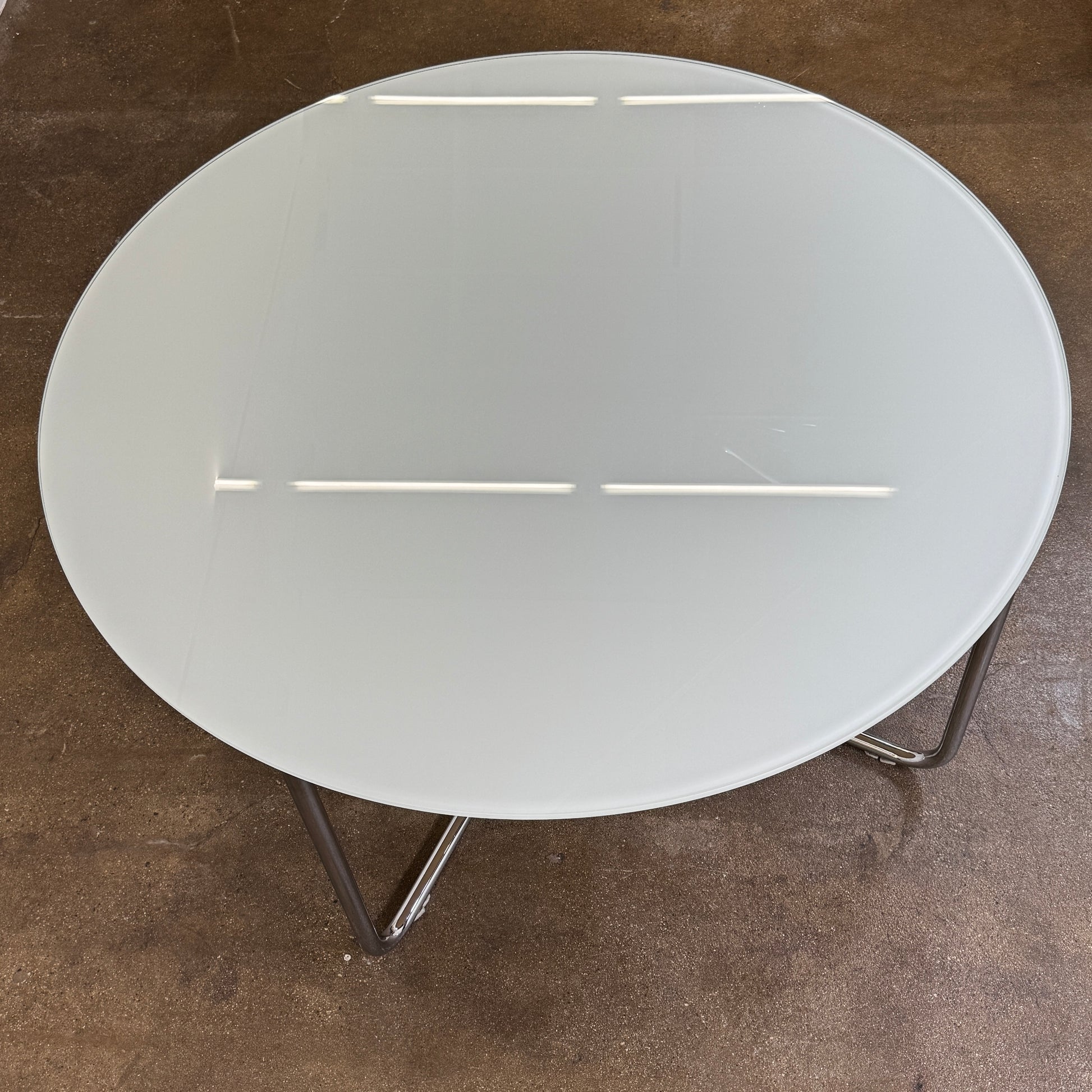 The Minotti Louis Round Dining Table features a white top and a modern metal base with three intersecting legs, reflecting Minotti’s signature style.